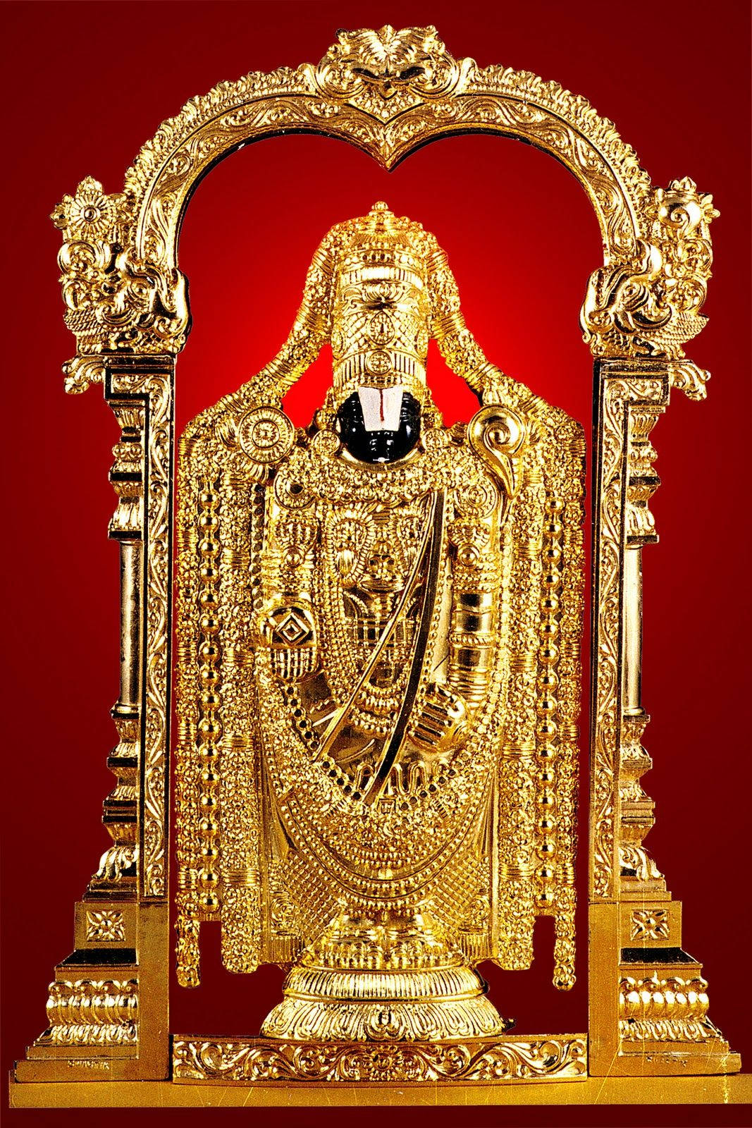 Venkateswara 桌布 壁紙 — 一尊閃耀的金色神像，飾有精緻珠寶和一把劍，矗立在裝飾華麗的拱門內，背景是深紅色。