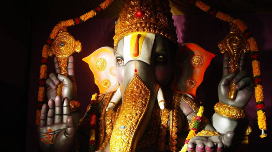 Hindu God 桌布 壁紙 — 一尊閃耀的金色象神像，飾以精緻珠寶和花環，襯托在深色背景上。