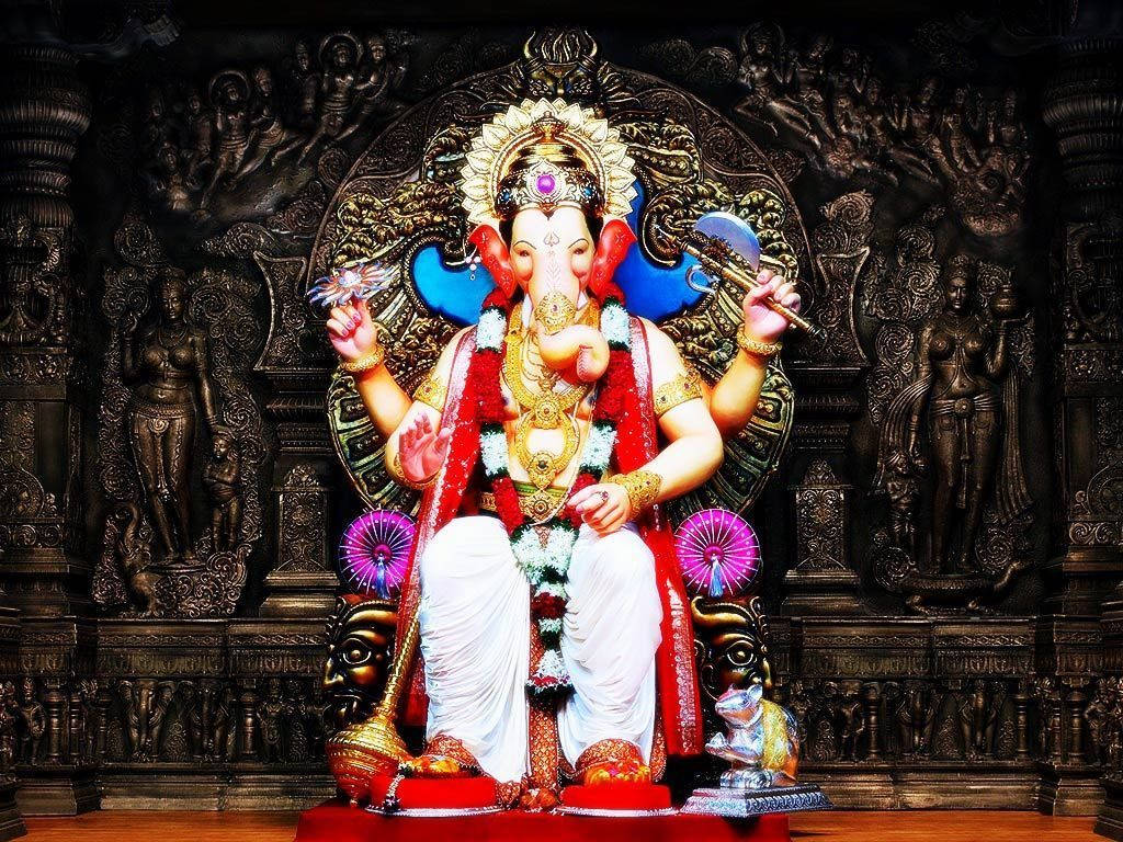 Hindu Temple 桌布 壁紙 — 一尊閃耀的金色象神像，飾以紅花和珠寶，莊嚴地坐在華麗的寶座上，背景是深色雕刻。