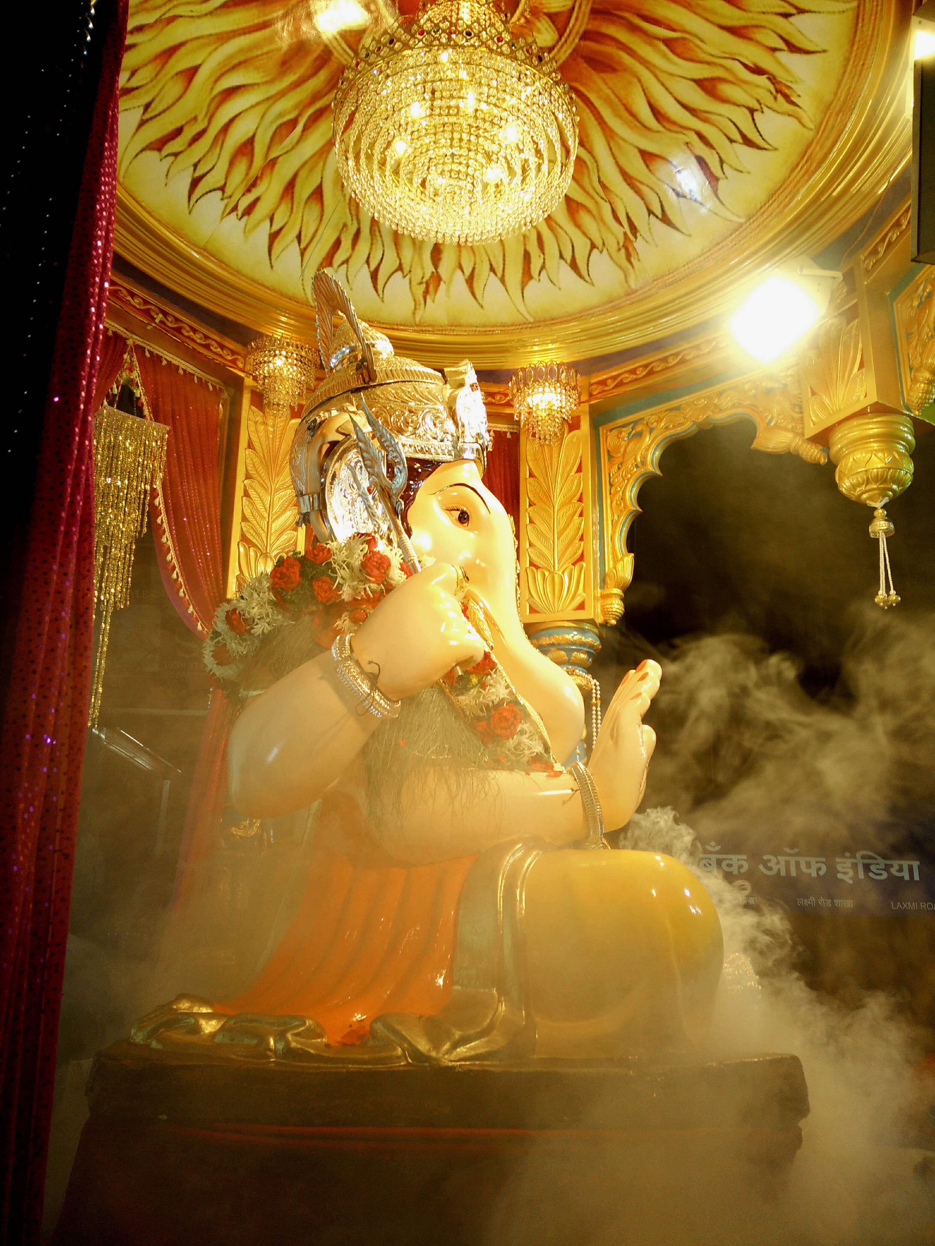 Bappa 桌布 壁紙 — 一尊閃耀的金色象神像端坐於陽光穿透的天花板下，沐浴在溫暖光線與旋轉迷霧之中。
