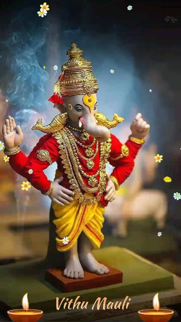 Indian 桌布 壁紙 — 一尊閃耀的金色象神雕像，身穿紅黃長袍，飾以珠寶和鮮花，立於煙霧繚繞的神秘背景前。