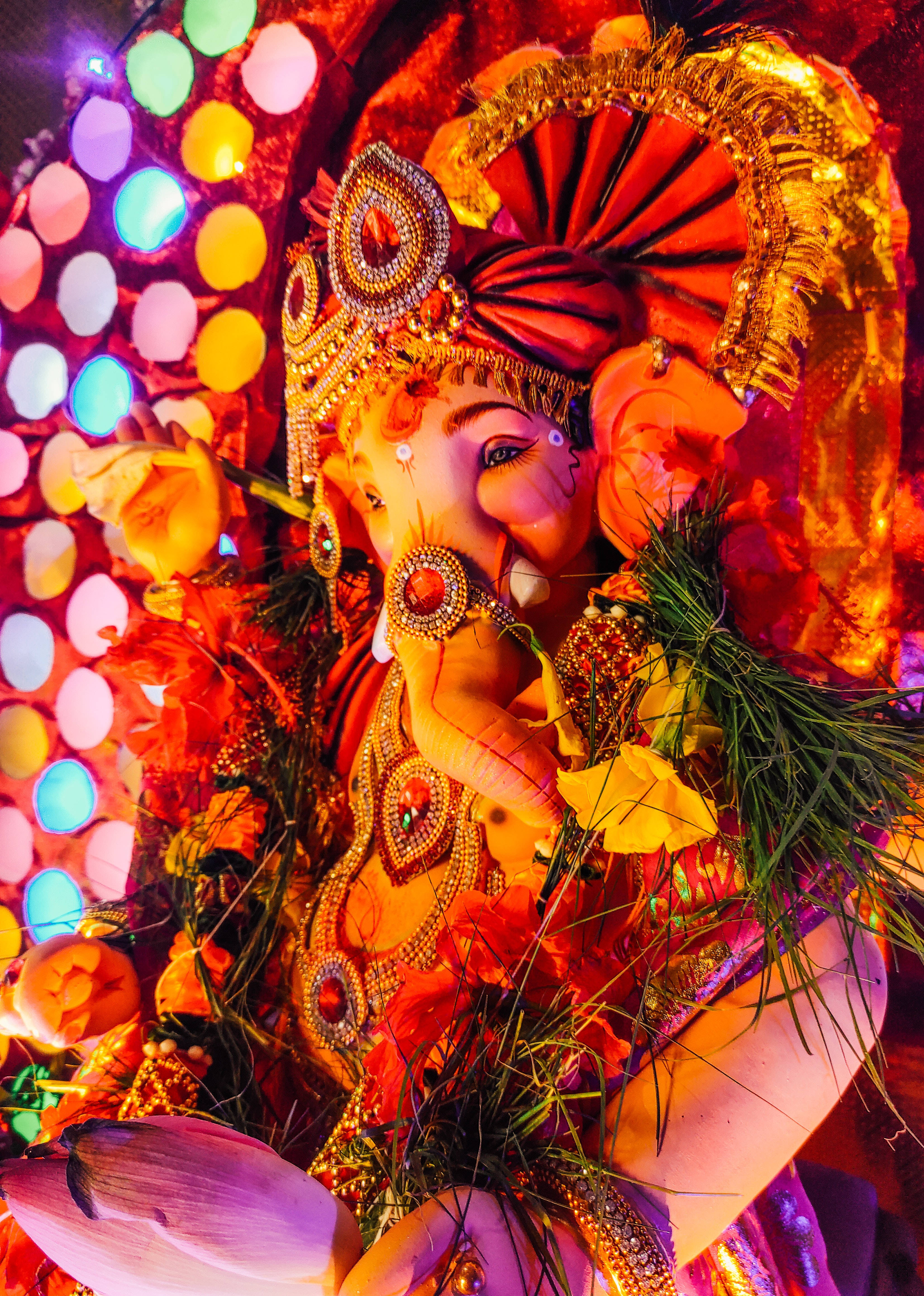 ganesh 4K 桌布 壁紙 — 一尊閃耀的金色象神雕像，飾有珠寶和鮮花，在彩色燈光的背景下閃閃發光。