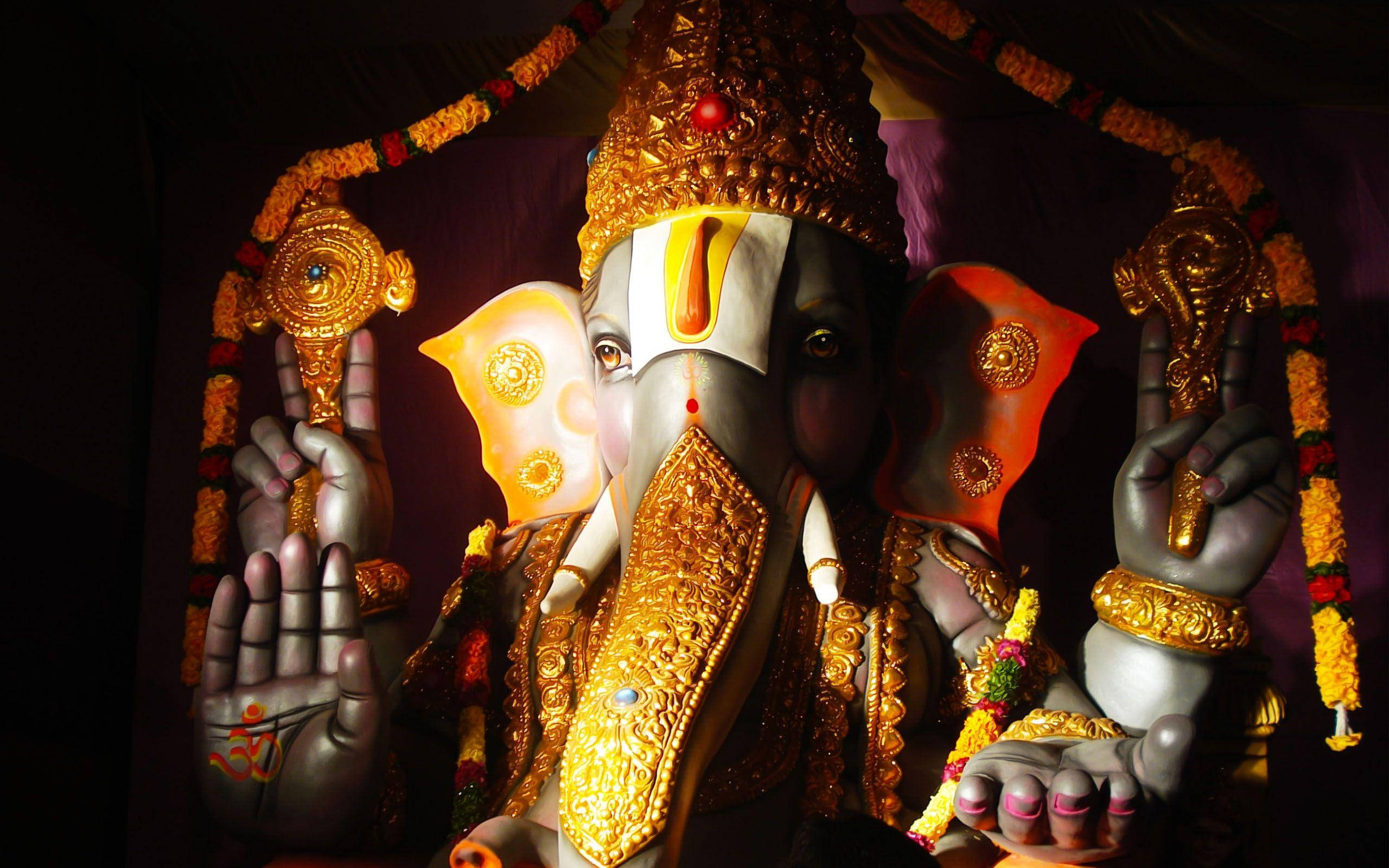 ganpati HD 桌布 壁紙 — 一尊閃耀的金色象頭神像，在戲劇性燈光下飾有花環和精緻珠寶。