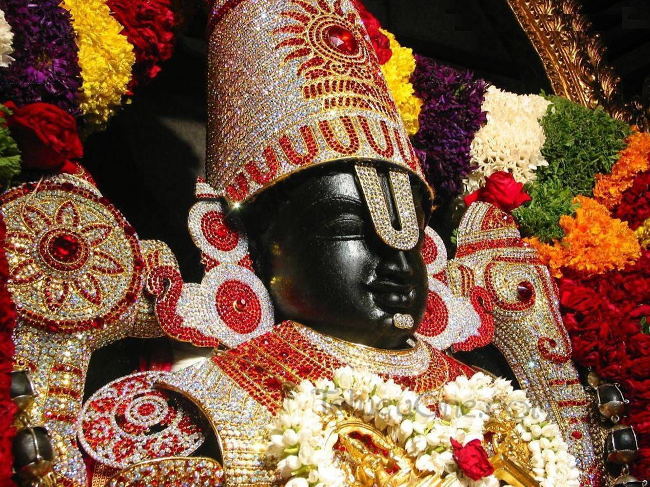 Hindu God 桌布 壁紙 — 一尊閃耀的黑色神像，飾以精緻的紅金和白色珠寶飾物，周圍環繞著鮮豔的花環。