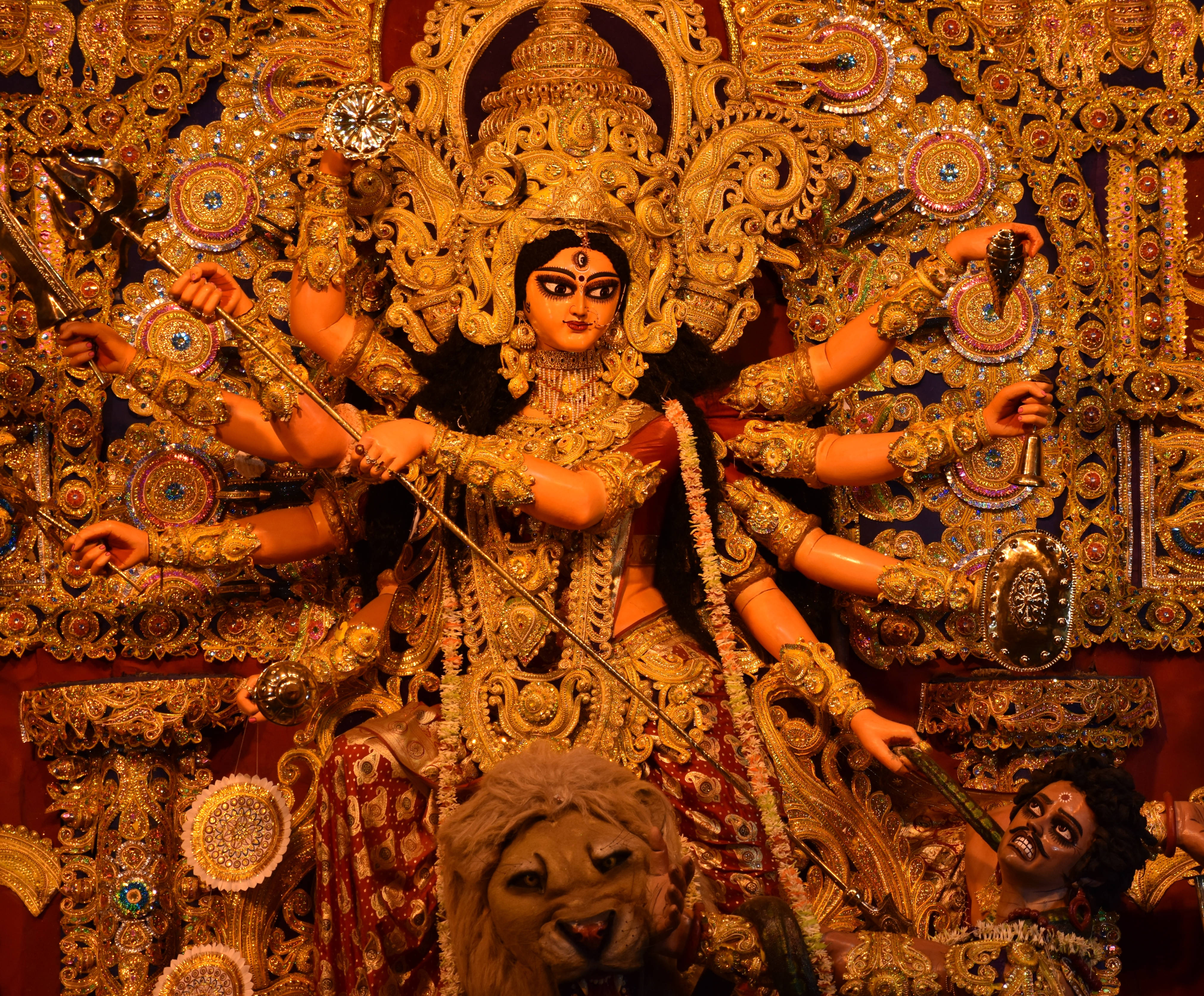 Goddess Kali 桌布 壁紙 — 一尊閃耀金色光芒、多臂持武器的杜爾迦雕像，在華麗背景前威嚴矗立。