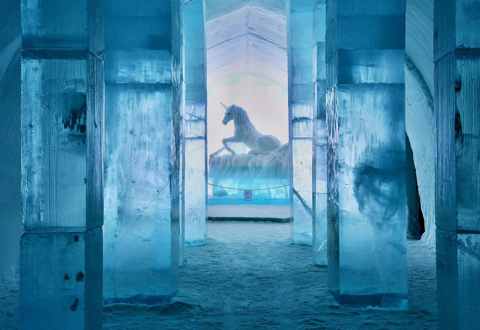 Ice Hotel 桌布 壁紙 — 一尊雄偉的白色獨角獸雕像安放在冰上，位於宏偉的冰之大教堂內，被柔和的藍光照亮。