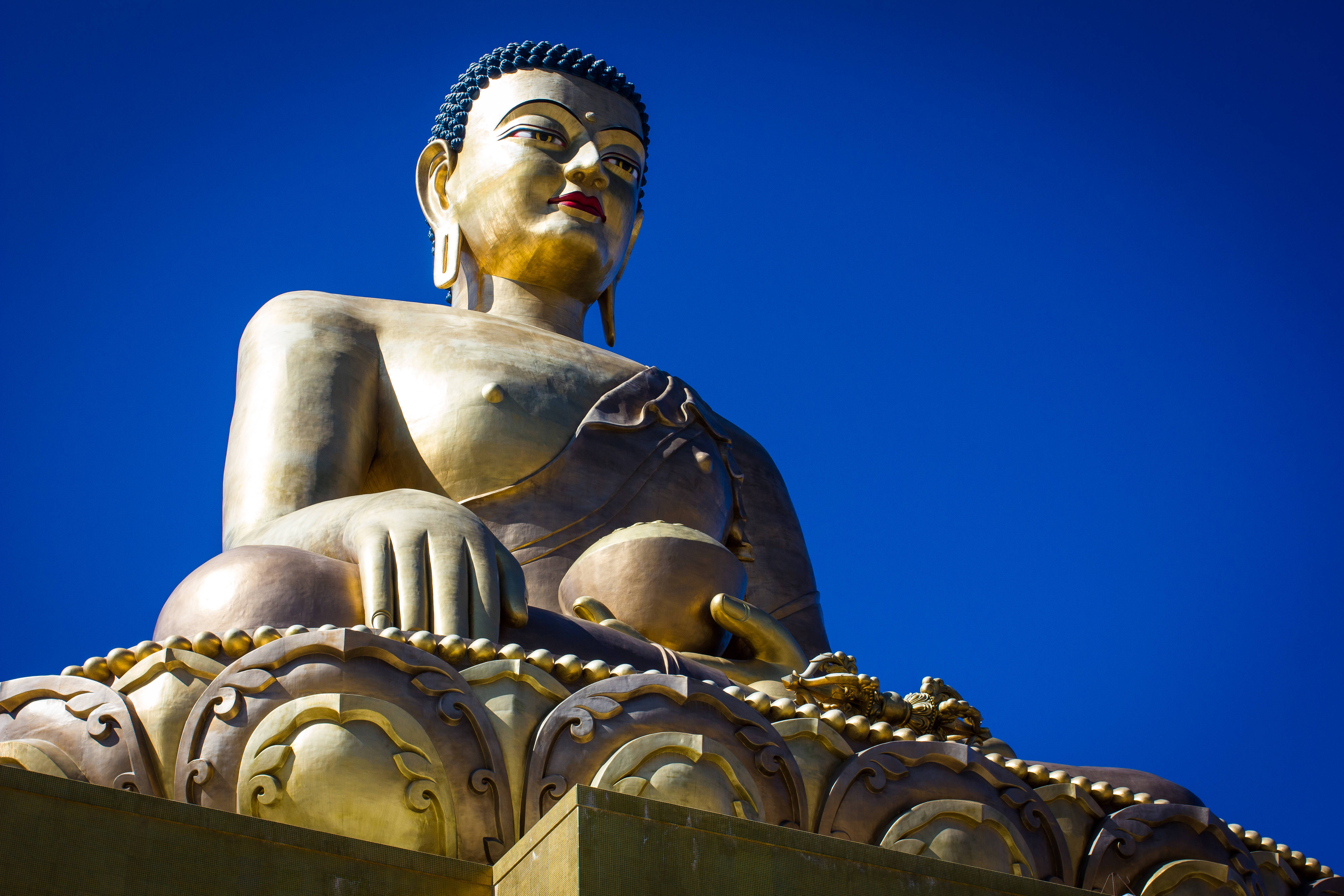 Bhutan 桌布 壁紙 — 一尊雄偉的金色佛像在鮮豔的藍天下靜坐，散發著和平與靈性的寧靜。