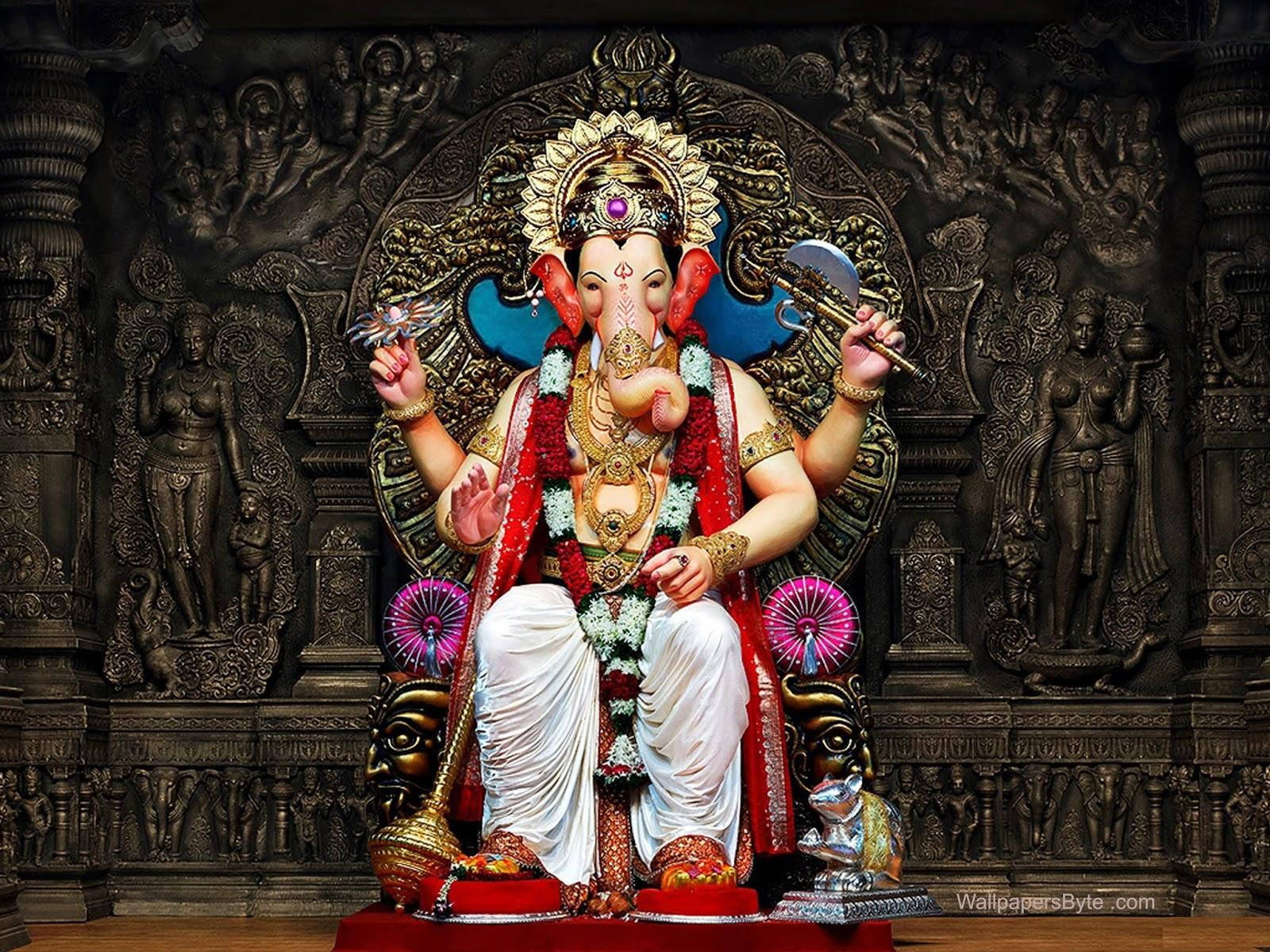 Ganesh 桌布 壁紙 — 一尊雄偉的金色象神雕像，飾有紅色花環和珠寶，莊嚴地坐在華麗的寶座上，背景是深色雕刻的寺廟。