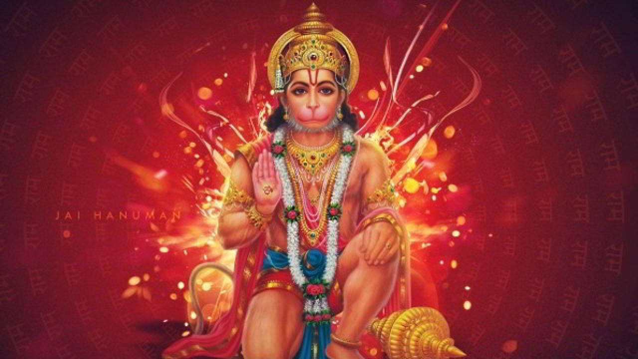 Hanuman Jayanti 桌布 壁紙 — 一尊雄偉的金飾哈努曼以強而有力的姿勢坐在光芒四射的紅色背景前，背景有發光粒子和梵文經文。