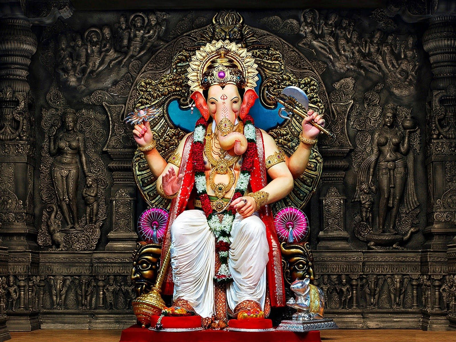 ganpati HD 桌布 壁紙 — 一尊雄偉的黃金象神像，飾有紅色花環和珠寶，威嚴地坐在華麗的寶座上，背景是深色雕刻的寺廟。