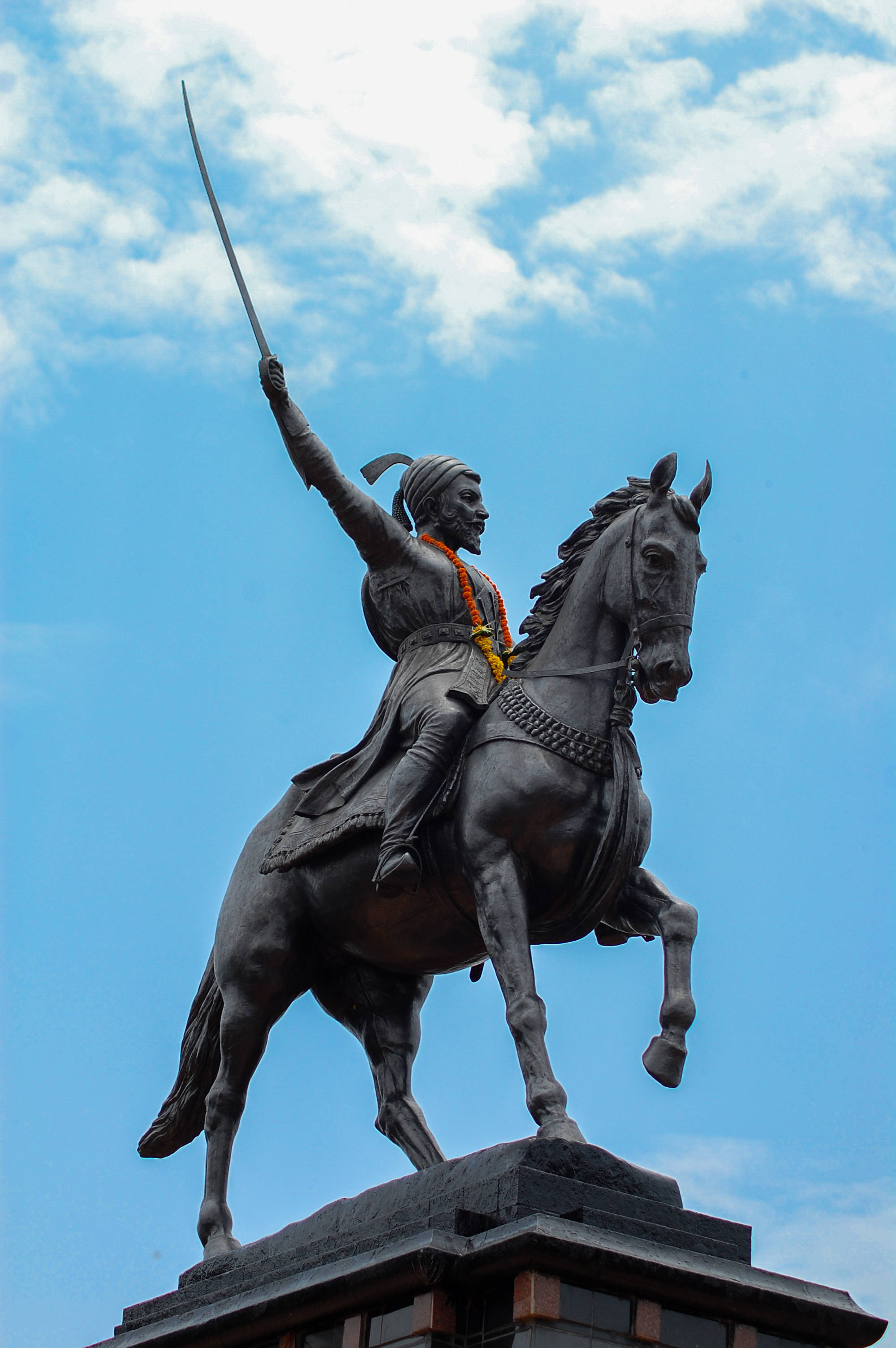 Chhatrapati Shivaji Maharaj 桌布 壁紙 — 一尊青銅騎馬戰士雕像，高舉寶劍，背景是明亮藍天，點綴著幾朵白雲。
