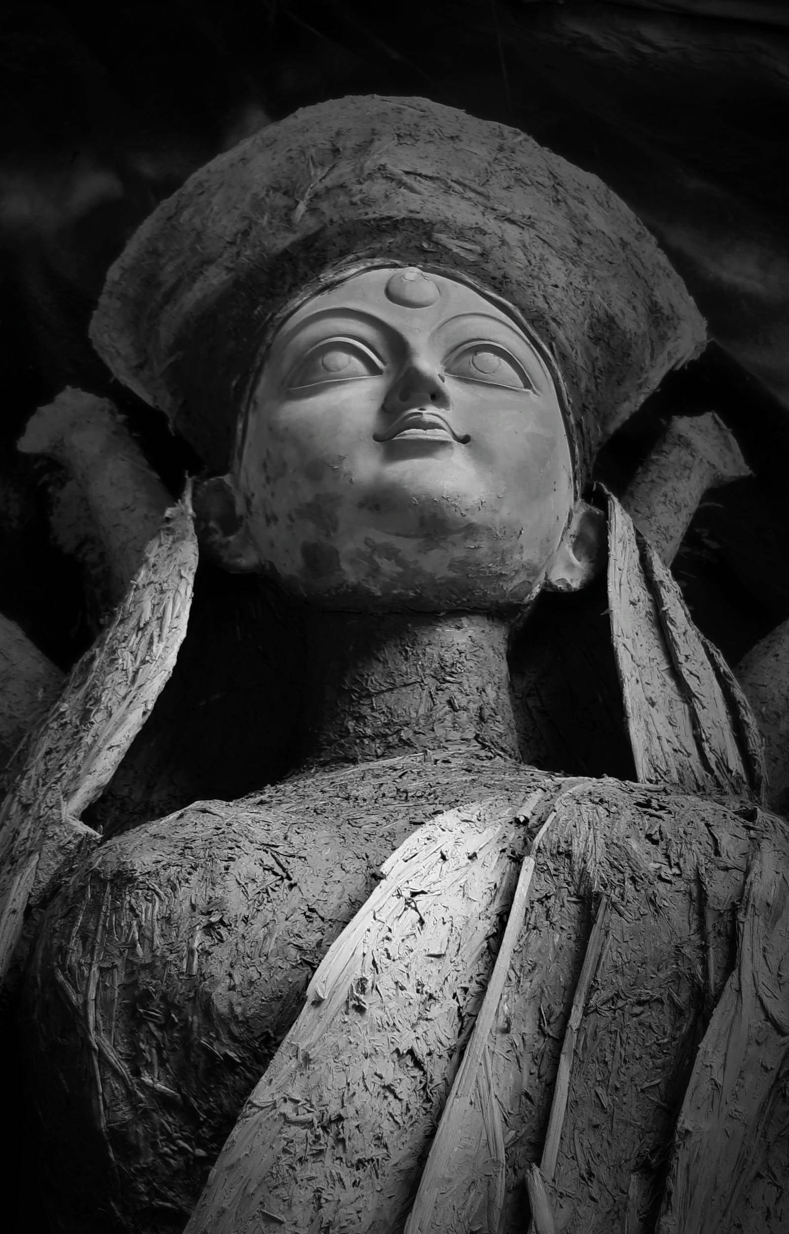 maa durga 桌布 壁紙 — 一尊風化的黑白佛像頭像，頭戴皇冠，身披垂褶長袍，在戲劇性的低光下拍攝。