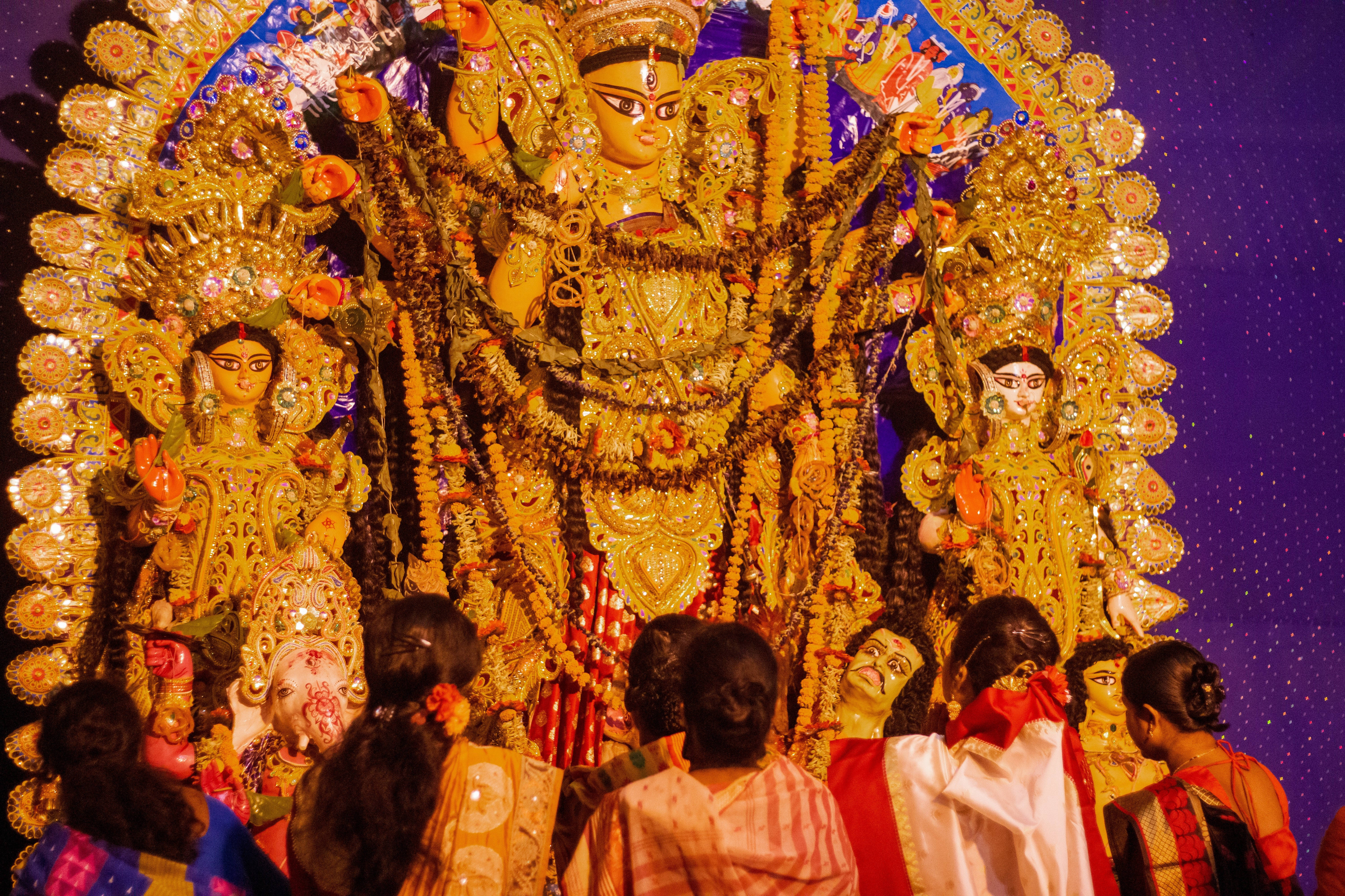 maa durga 桌布 壁紙 — 一尊飾有珠寶和鮮花的金色杜爾加普迦神像在夜間被照亮，信徒們恭敬地鞠躬。