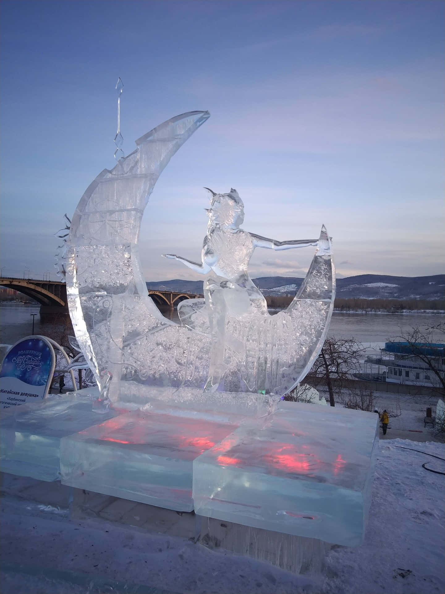 Ice Sculpture 桌布 壁紙 — 一尊騎著新月的神話生物的雄偉冰雕，在黃昏時分，在白雪皚皚的河邊發出紅光。