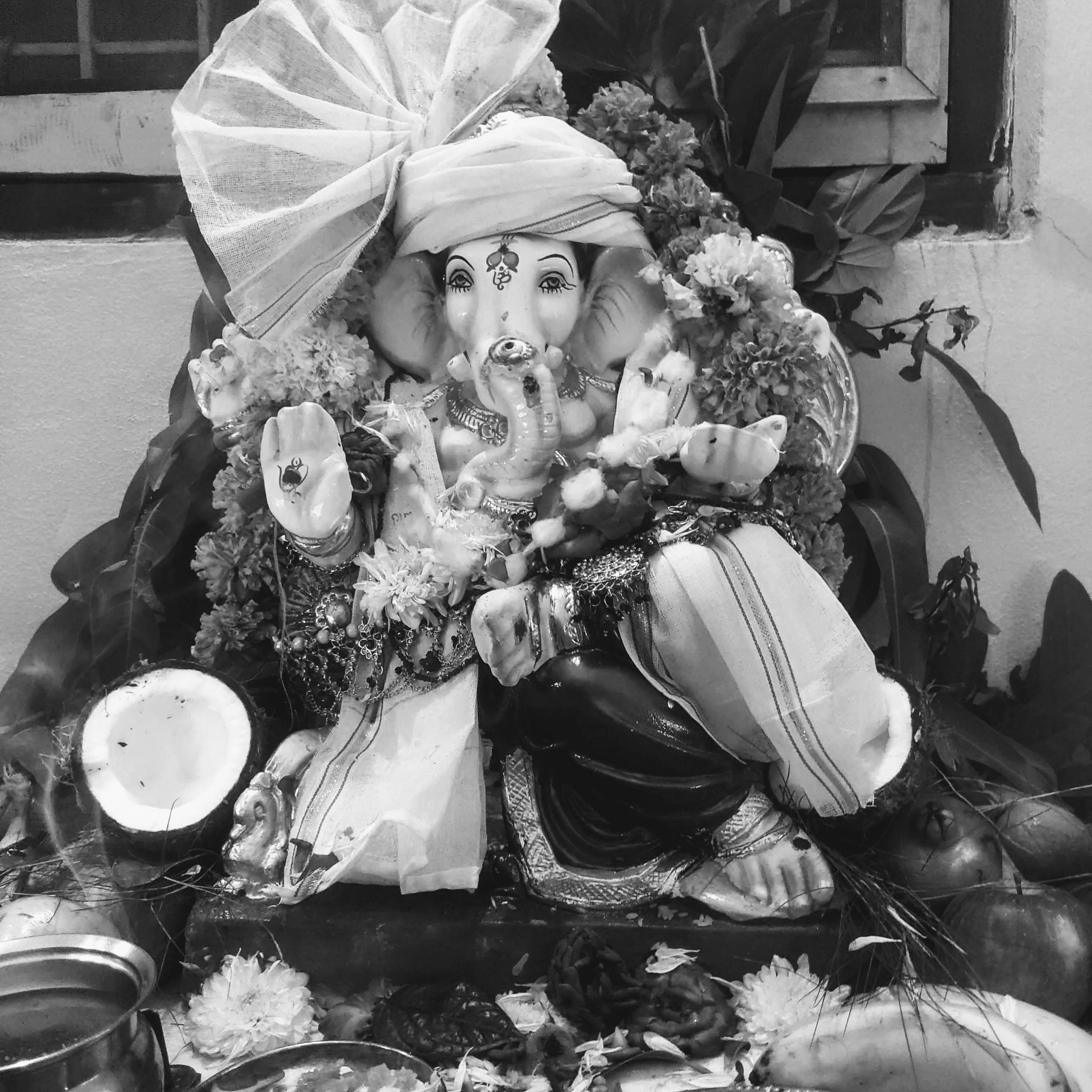 Ganesh 桌布 壁紙 — 一尊黑白相間的象神雕像，飾以鮮花和供品，安坐於裝飾華麗的祭壇上。