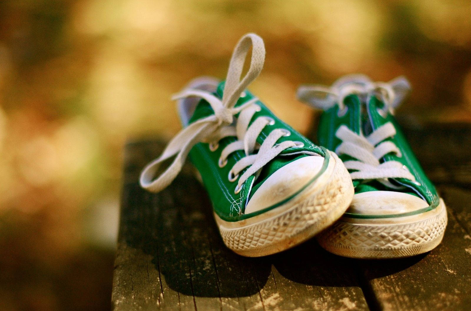 Green Shoes 桌布 壁紙 — 一對亮綠色帆布運動鞋搭配白色鞋帶，放置在經風化的木質表面上，背景是溫暖的金色散景。