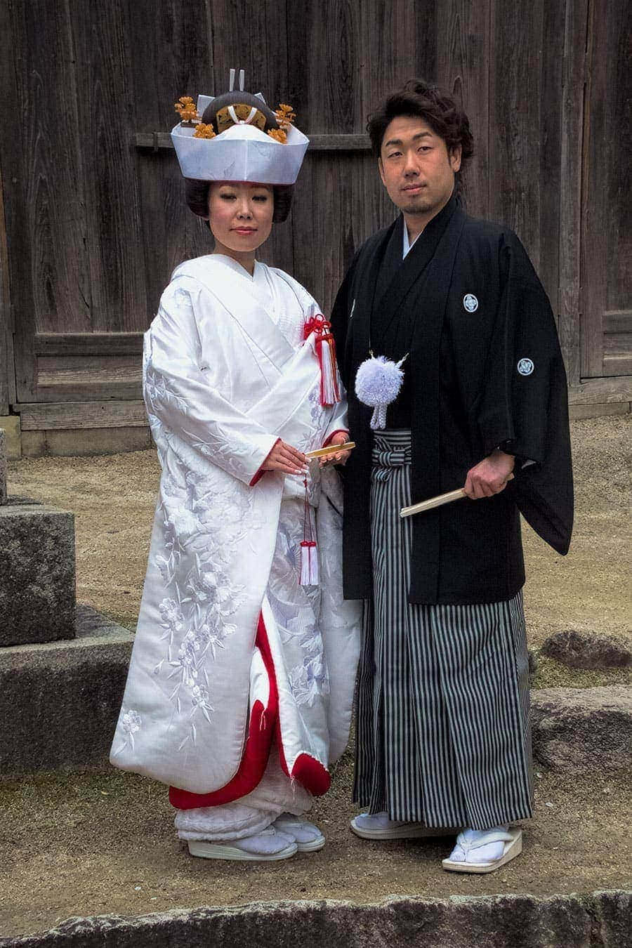 Kimono 桌布 壁紙 — 一對傳統日本新人穿著婚禮服飾，站在風化的木製神社門前。