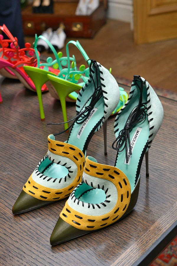 鞋子 桌布 壁紙 — 一對充滿活力的 Manolo Blahnik 高跟鞋，採用黃綠色和藍綠色麂皮，搭配黑色縫線，放在木桌上，背景是色彩繽紛的鞋子。