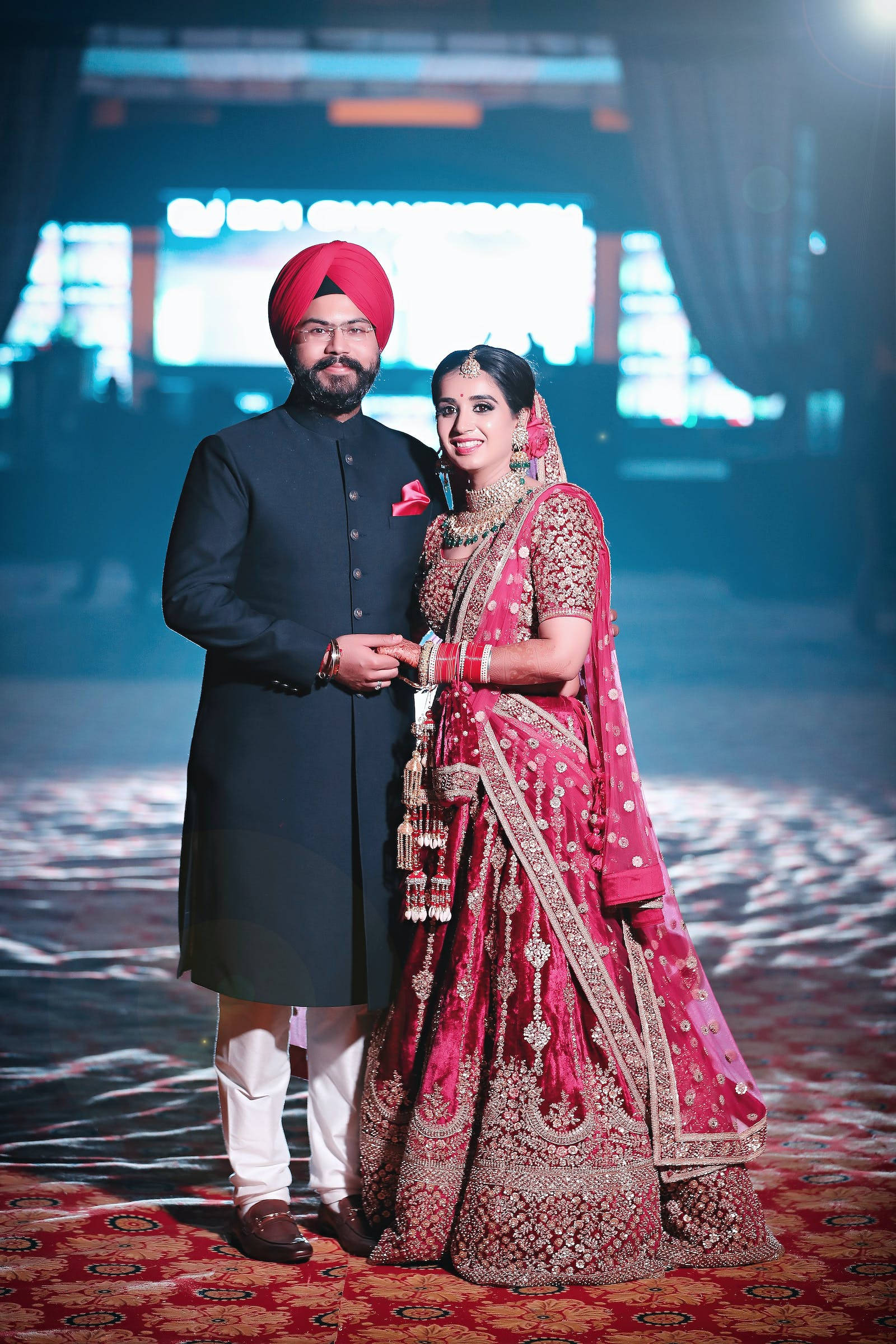 Indian 桌布 壁紙 — 一對光芒四射的印度情侶穿著傳統婚禮服飾，在戲劇性的舞台燈光下一起擺姿勢。