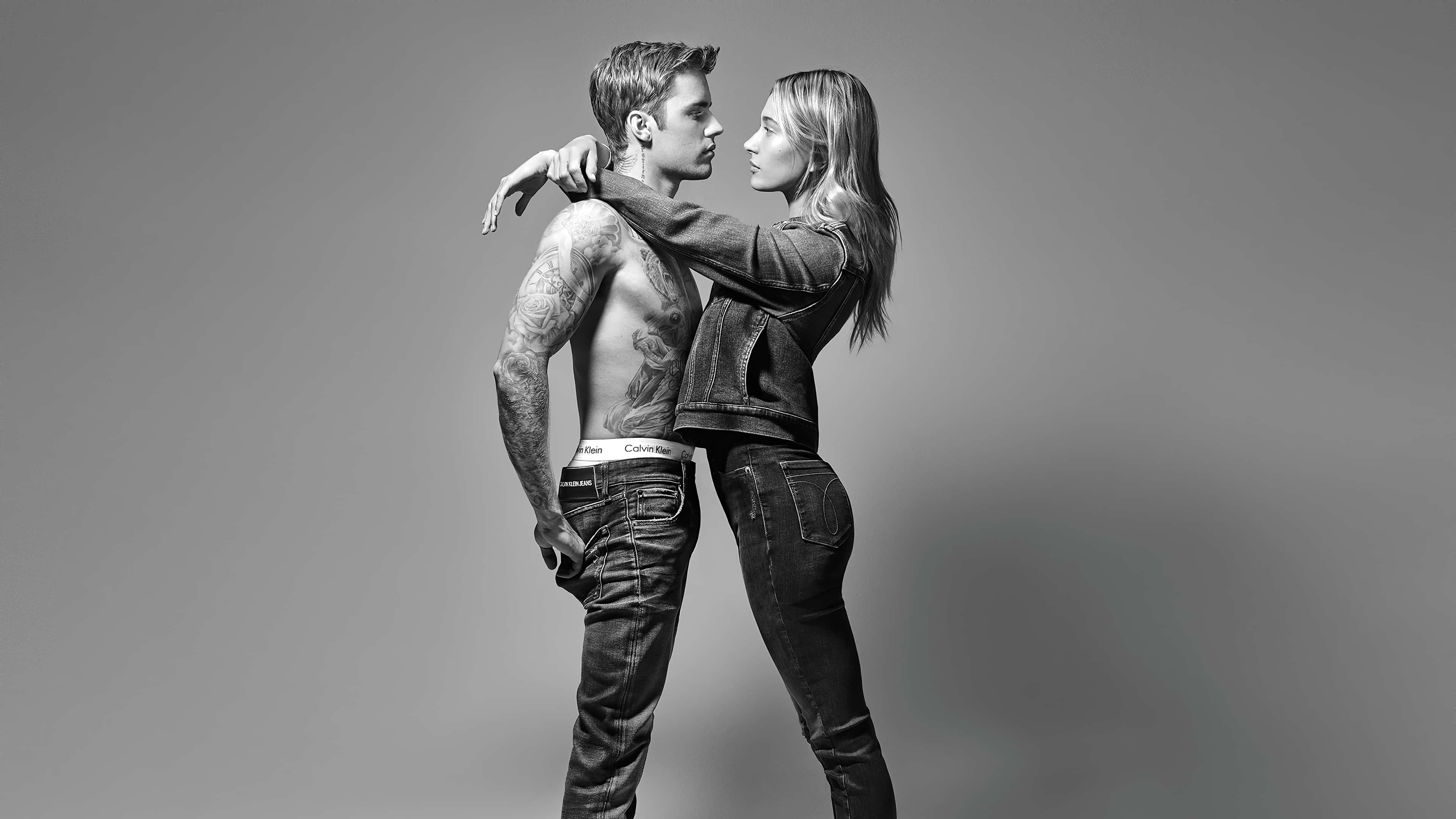 Justin Bieber 2021 桌布 壁紙 — 一對刺青男女穿著牛仔褲，在純灰色背景前緊密站立的黑白工作室肖像。