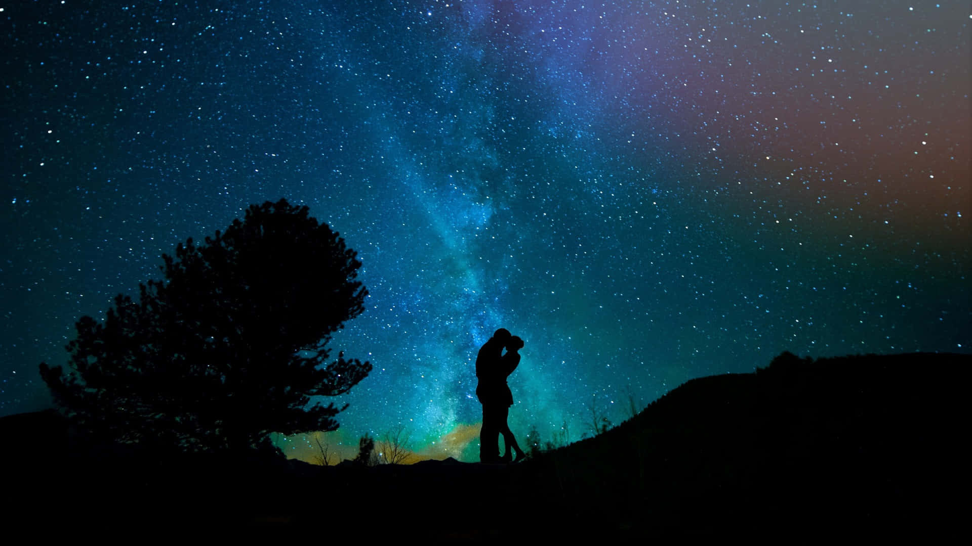 Starry Sky 桌布 壁紙 — 一對剪影情侶在充滿活力的星空下擁抱，銀河在一棵孤樹上方閃耀。