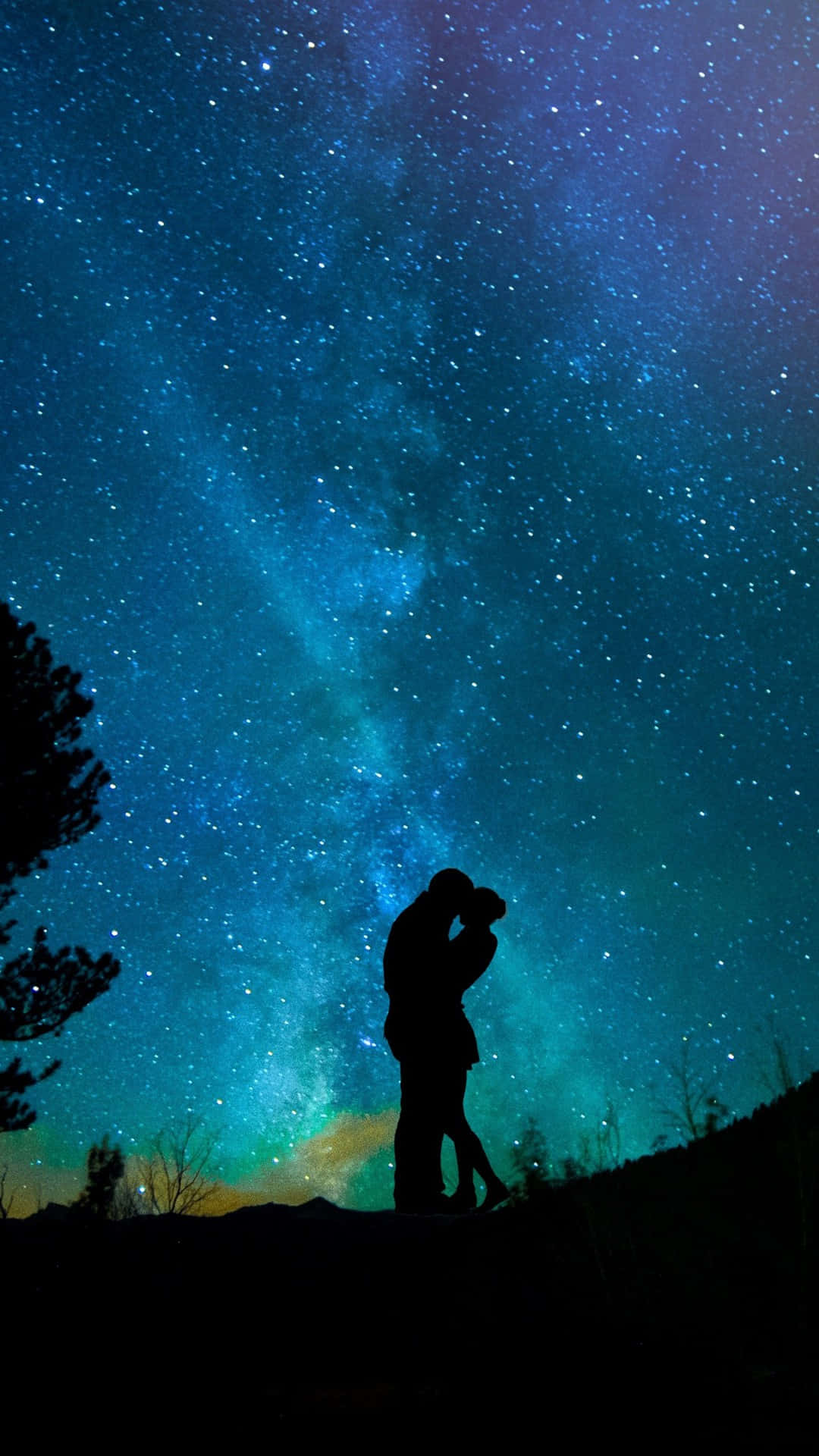情侶 桌布 壁紙 — 一對剪影情侶在壯麗的星空下擁抱，天空中有鮮豔的藍色和藍綠色星雲。