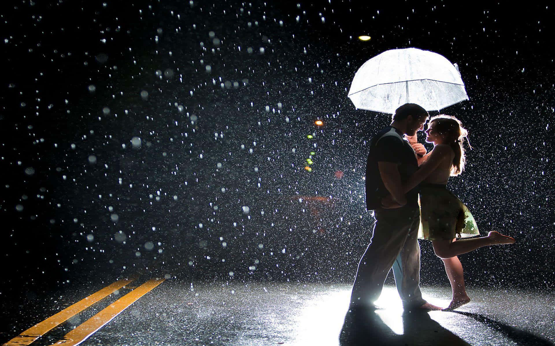 Couple In Rain 桌布 壁紙 — 一對剪影情侶在昏暗濕滑的街道上，在傾盆大雨中於發光的雨傘下跳舞，背景是模糊的城市燈光。