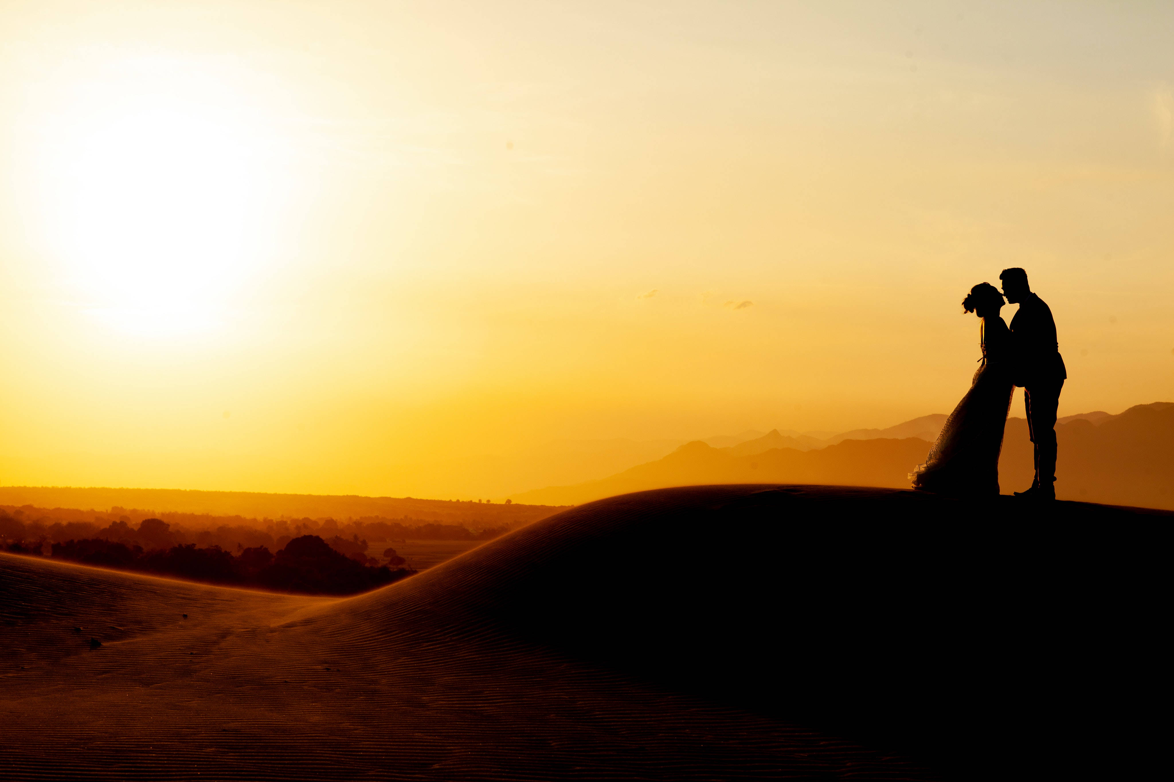 Silhouette 桌布 壁紙 — 一對剪影情侶在沙漠沙丘頂上親吻，夕陽在金色天空中落下。