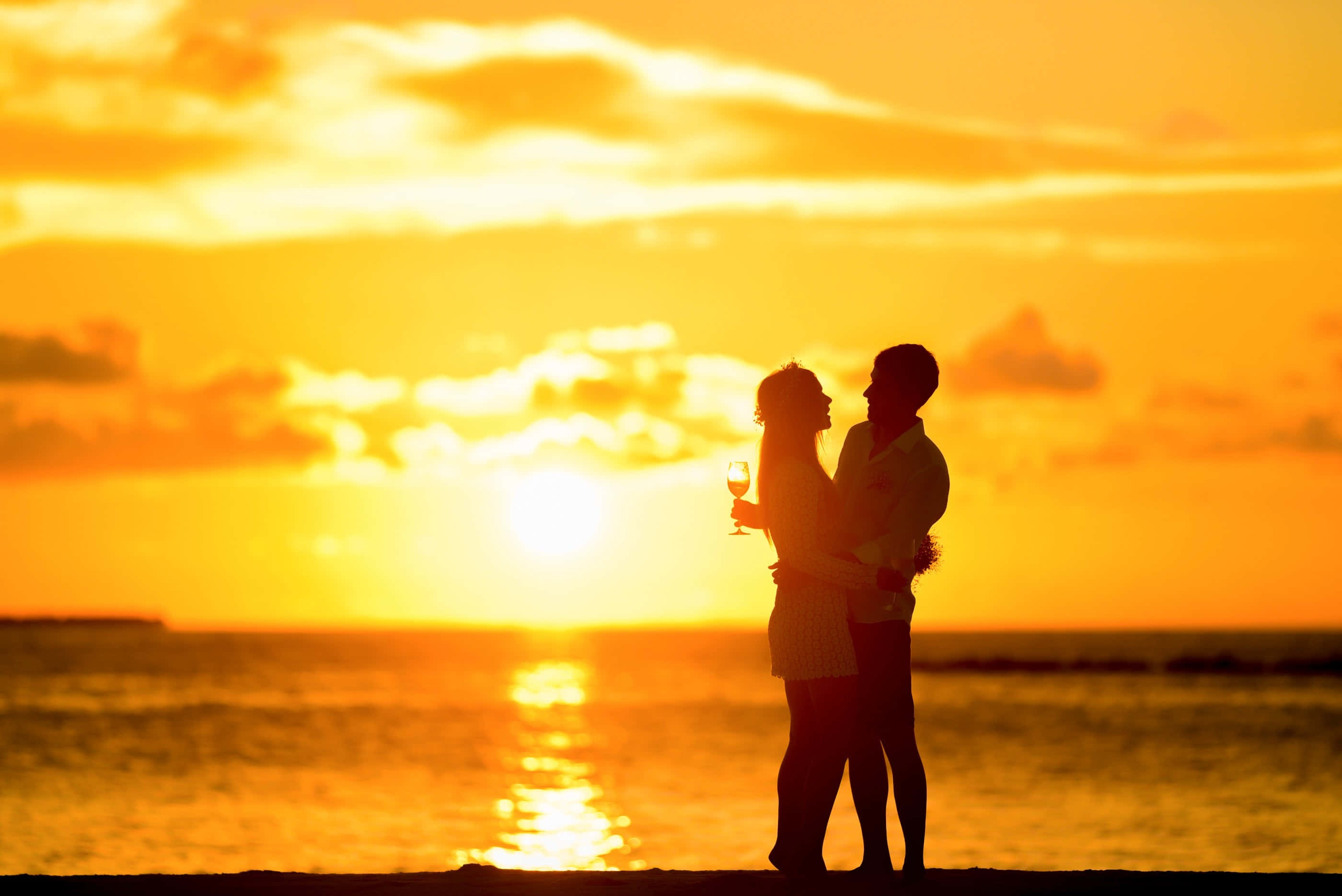 Beach Love 桌布 壁紙 — 一對剪影情侶在海灘上擁抱，夕陽以火熱的橙色和金色色調沉入海洋。