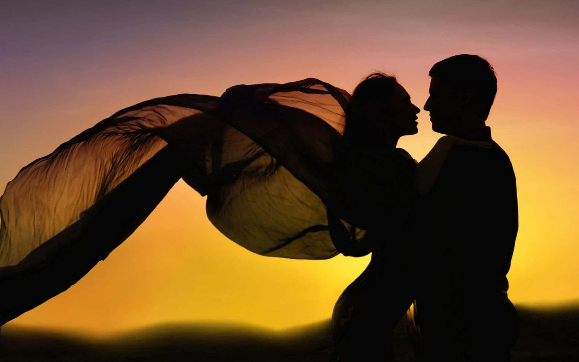 Romantic Love 桌布 壁紙 — 一對剪影情侶擁抱，飄逸的布料在溫暖的日落天空下戲劇性地飄揚。