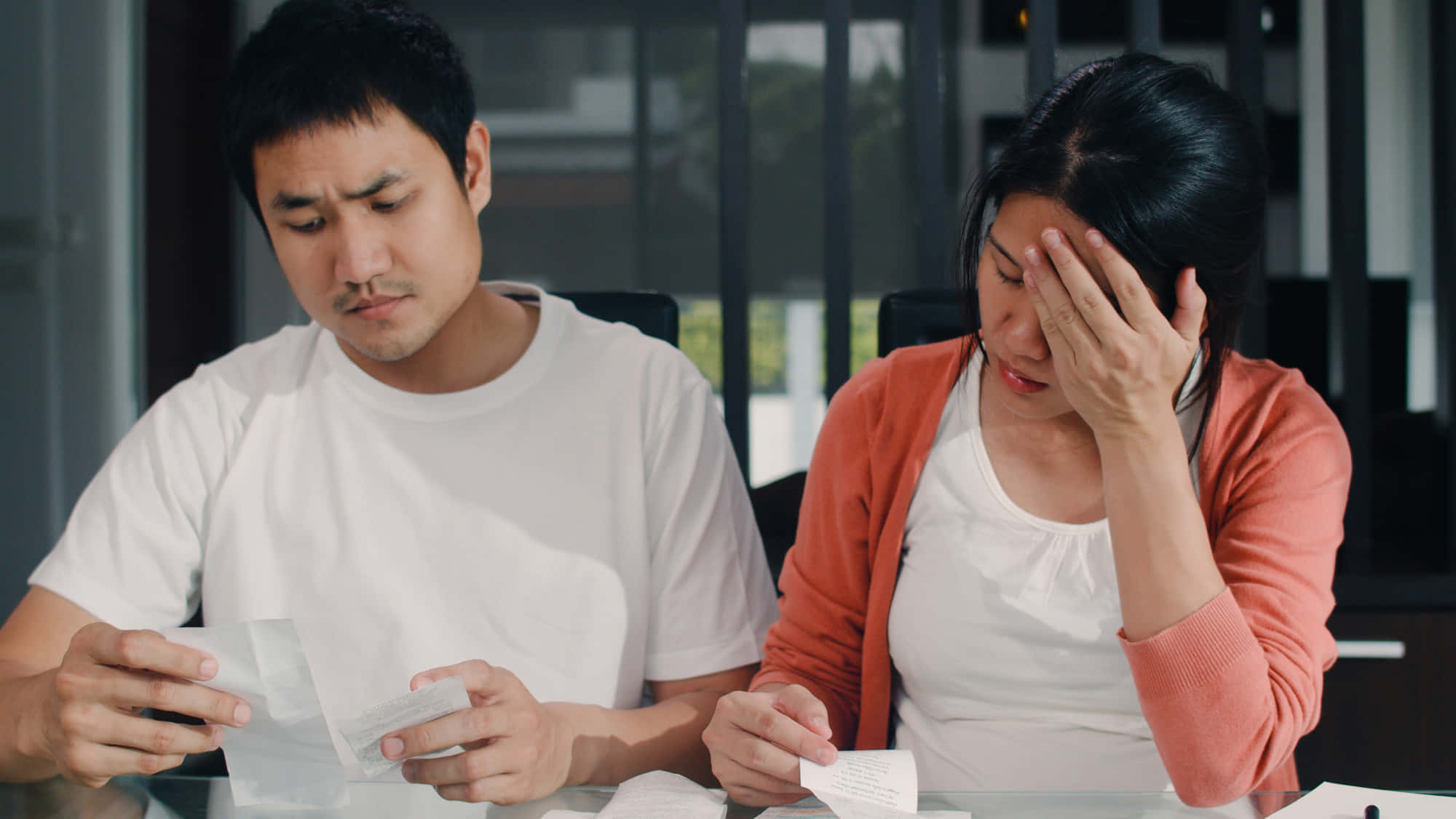 Bills 桌布 壁紙 — 一對壓力大的情侶坐在桌旁，帶著憂慮的表情查看帳單，其中一名女子因沮喪而抱頭。