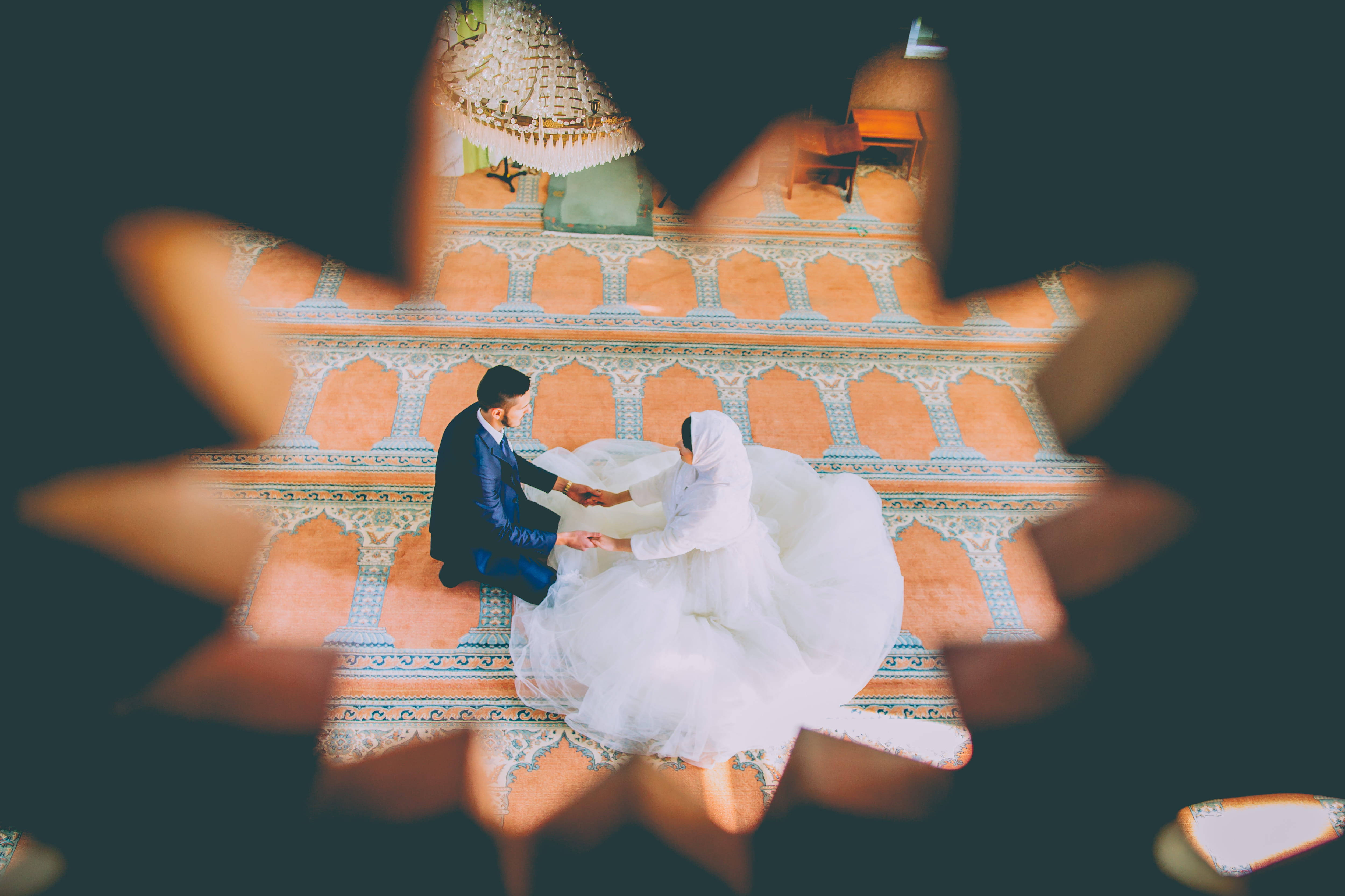 Wedding Dress 桌布 壁紙 — 一對夫婦在圖案清真寺地板上跪著祈禱，透過星形鏡頭光暈觀看。