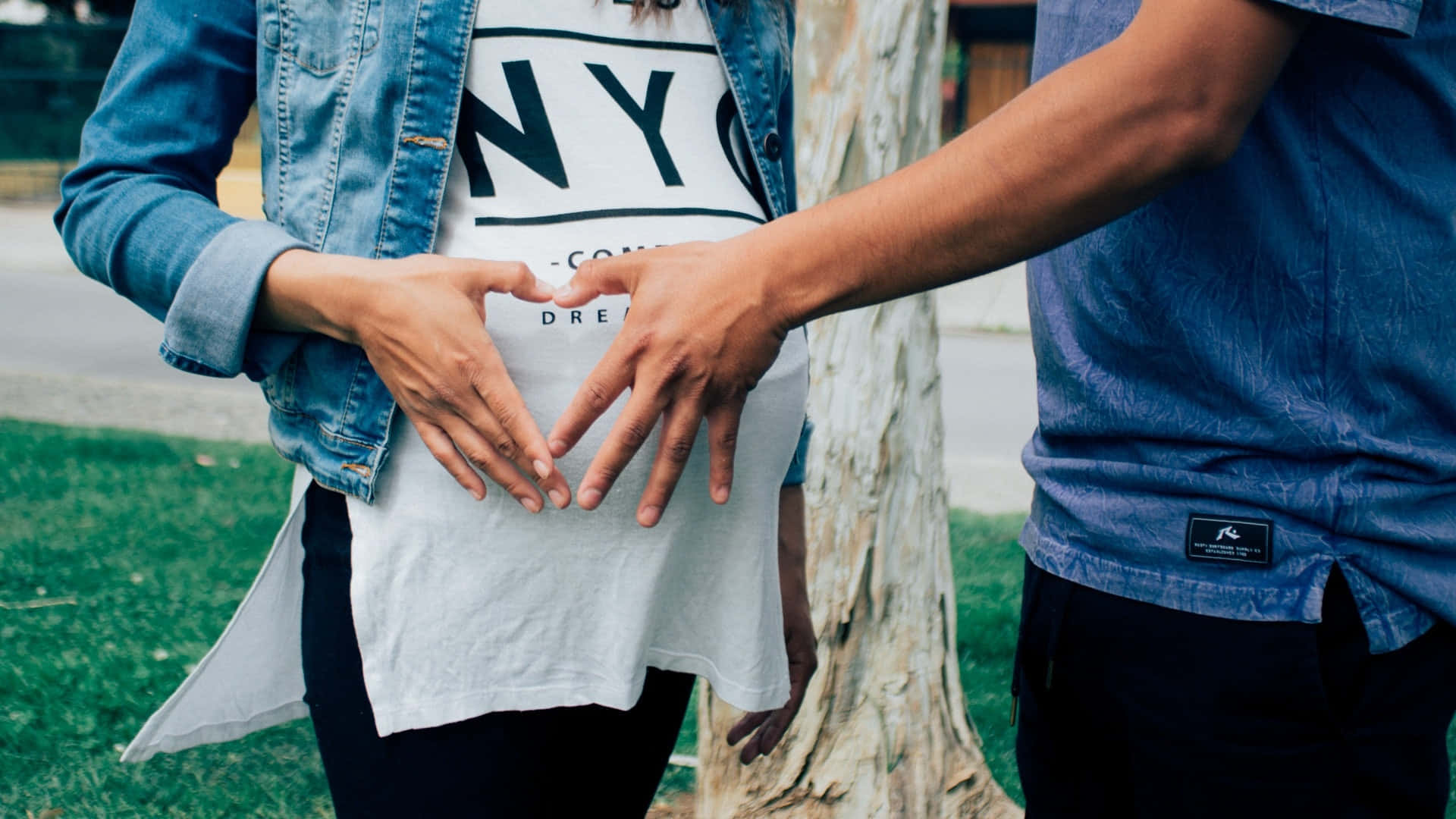 Pregnant 桌布 壁紙 — 一對夫婦在戶外靠近樹木的地方，用手在懷孕的肚子上形成心形。