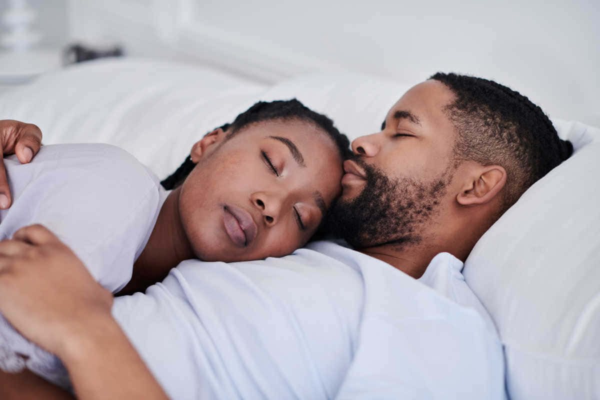 Black Couple 桌布 壁紙 — 一對平靜的情侶在明亮的白色臥室中並排入睡，他們的臉龐輕輕地靠在枕頭上。
