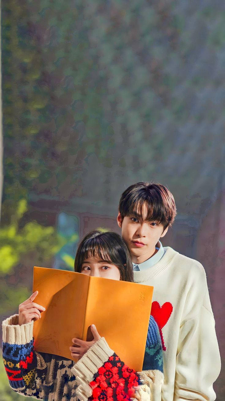 Couples 桌布 壁紙 — 一對年輕情侶分享一個嬉戲時刻，女孩躲在書本後面，男孩帶著溫柔的微笑看著她。