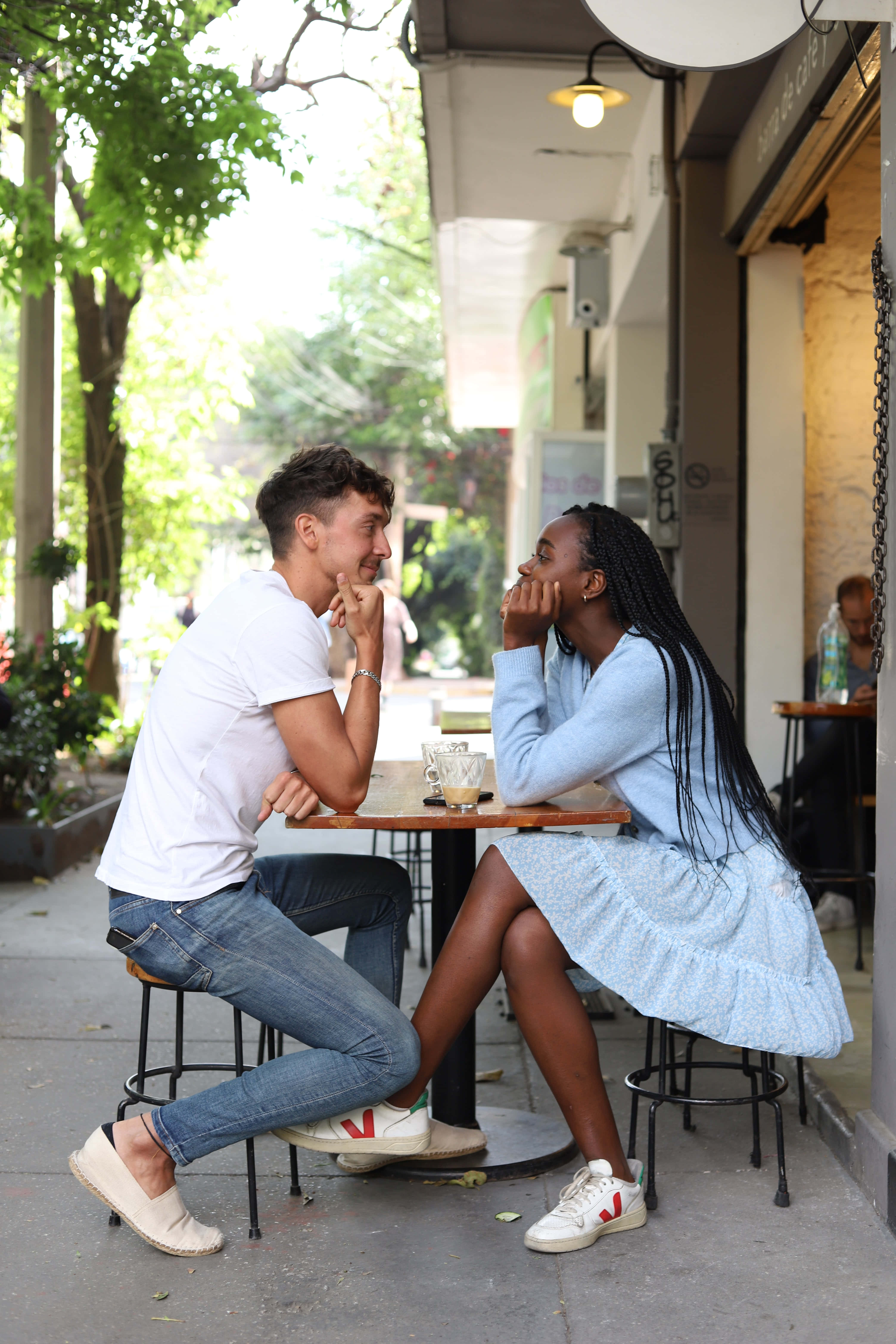 Interracial 桌布 壁紙 — 一對年輕情侶在明亮的日光下，於戶外咖啡桌分享親密對話。