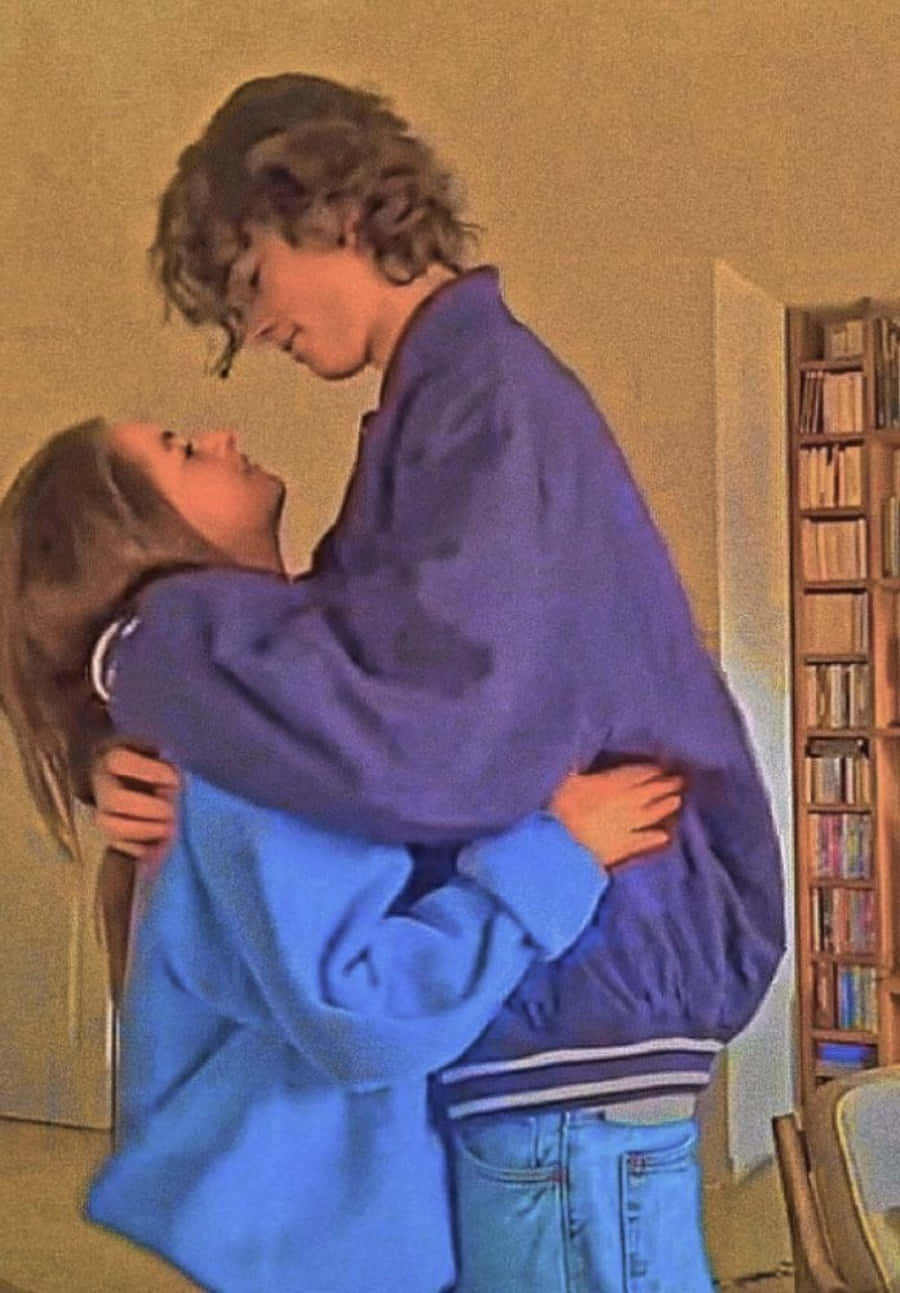 Cute Boyfriend 桌布 壁紙 — 一對年輕情侶在溫暖燈光的房間裡溫柔擁抱，背景有書架。