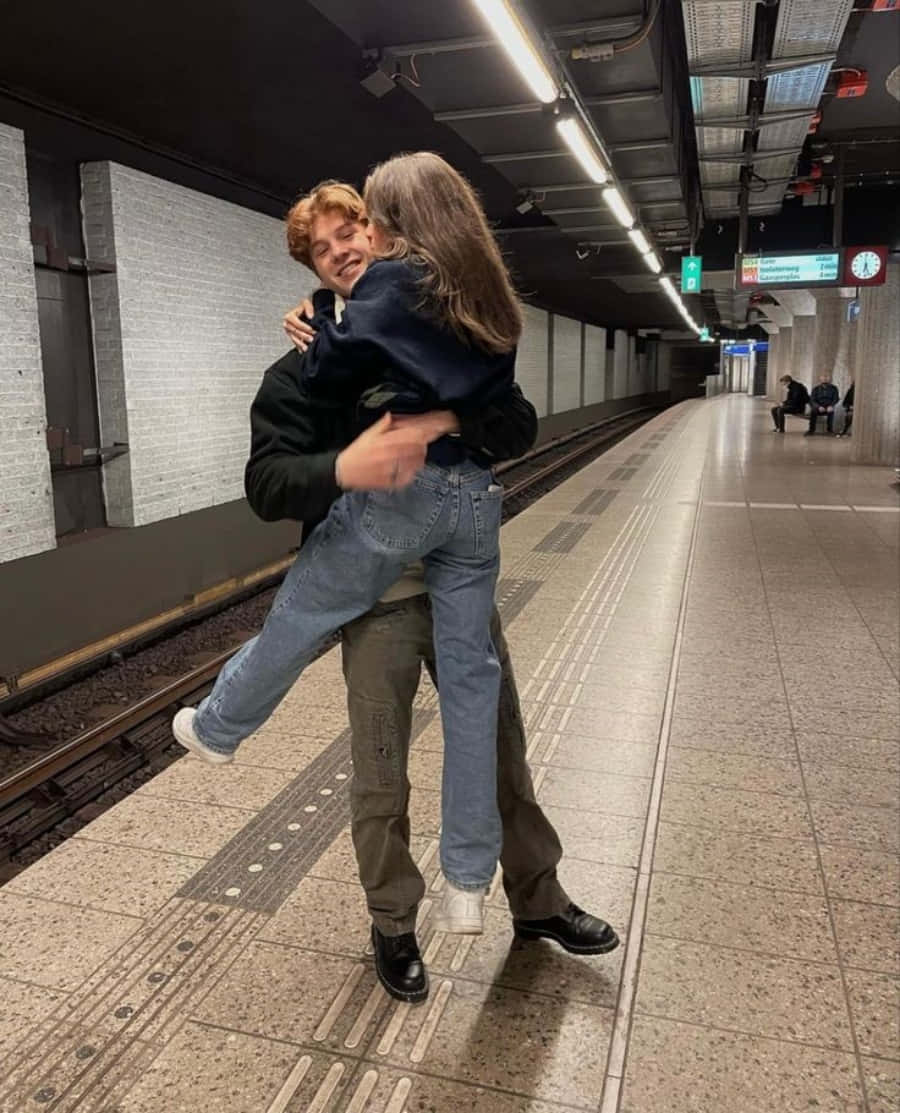 Aesthetic Couple 桌布 壁紙 — 一對年輕情侶在燈光昏暗的地鐵月台上熱情擁抱，背景有路軌和磁磚牆壁。