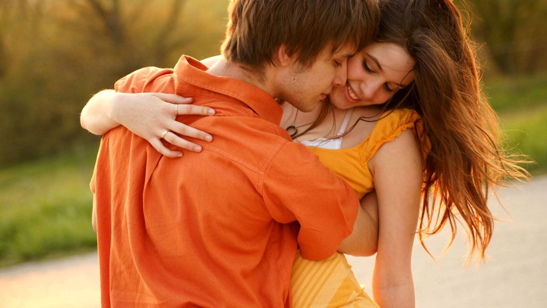 Romantic Love 桌布 壁紙 — 一對年輕情侶在金色夕陽下溫暖擁抱，身後是模糊的綠色植物。