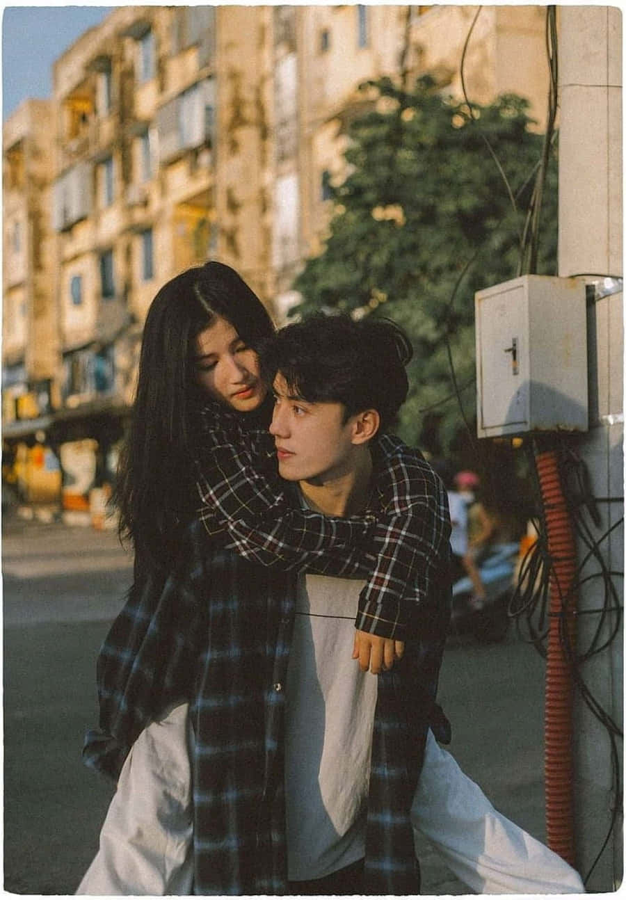 Boyfriend And Girlfriend 桌布 壁紙 — 一對年輕情侶在陽光明媚的城市街道上溫暖擁抱，背景是復古建築和綠植。