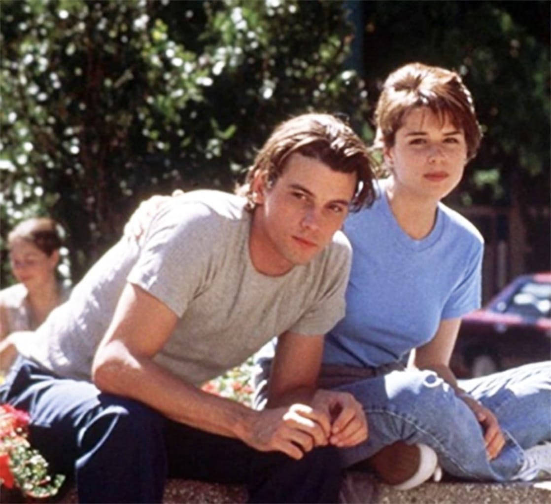 Billy Loomis 桌布 壁紙 — 一對年輕情侶在陽光明媚的日子裡，被綠樹和鮮花環繞，緊密地坐在一起。