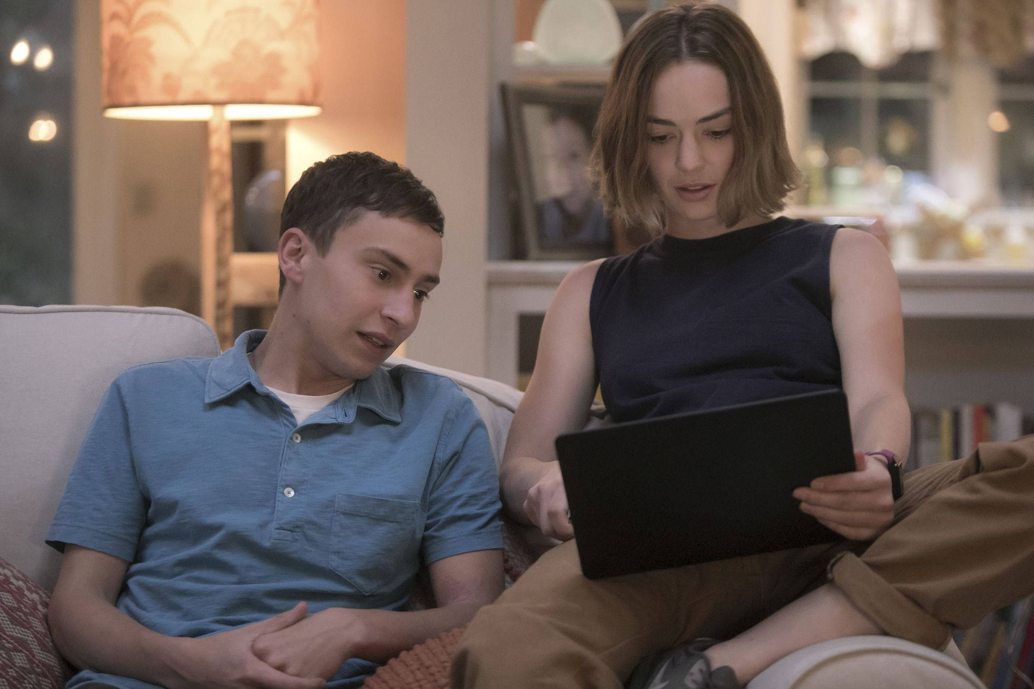 Netflix 桌布 壁紙 — 一對年輕情侶坐在溫暖照明的客廳沙發上，女子使用筆記型電腦，男子好奇地看著她。