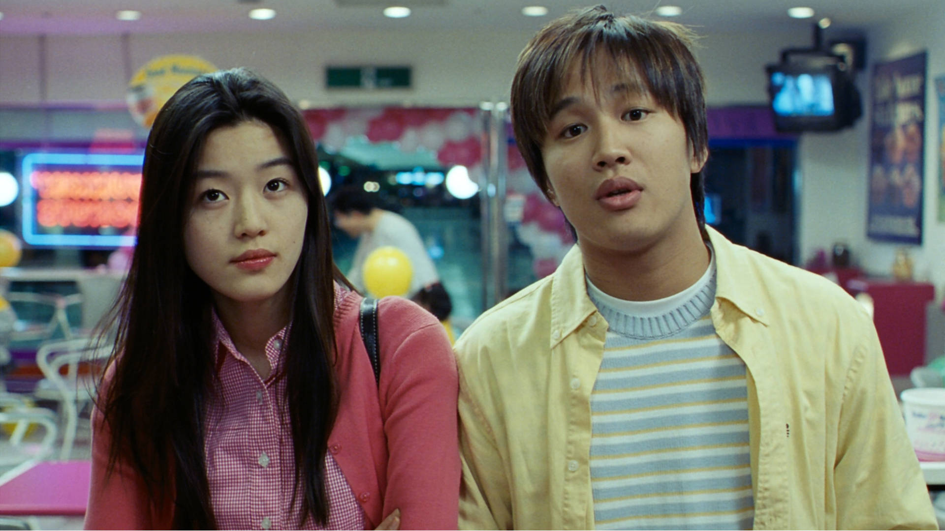 Jun Ji Hyun 桌布 壁紙 — 一對年輕情侶站在一個燈光明亮的遊戲機中心，身後有霓虹燈招牌和遊戲機。