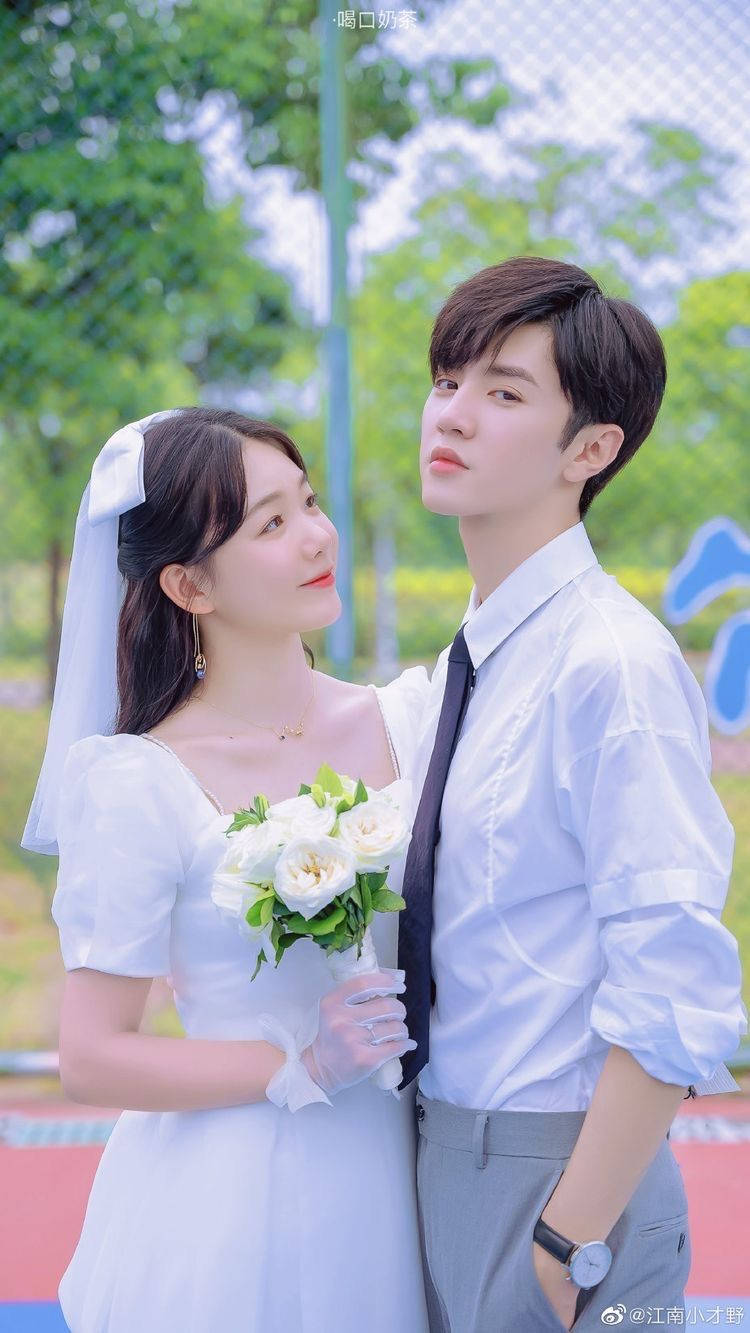 Wedding 桌布 壁紙 — 一對年輕新人穿著婚禮服裝，在運動場上靠近站立，上方是翠綠的樹木，柔和陽光穿透樹葉灑落。