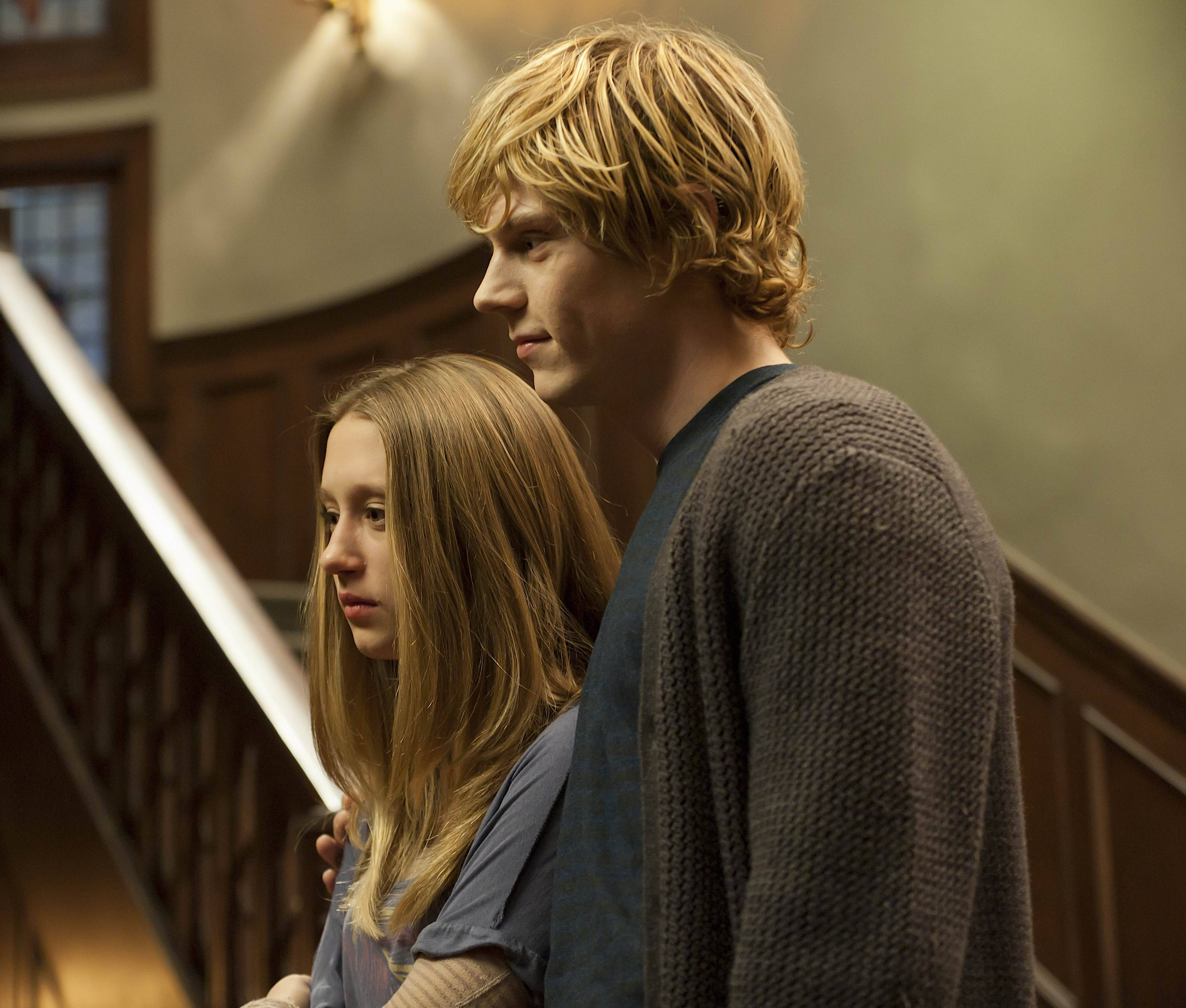 American Horror Story 桌布 壁紙 — 一對年輕男女並肩站在木樓梯上，室內燈光溫暖，兩人都以嚴肅的表情望向鏡頭外。