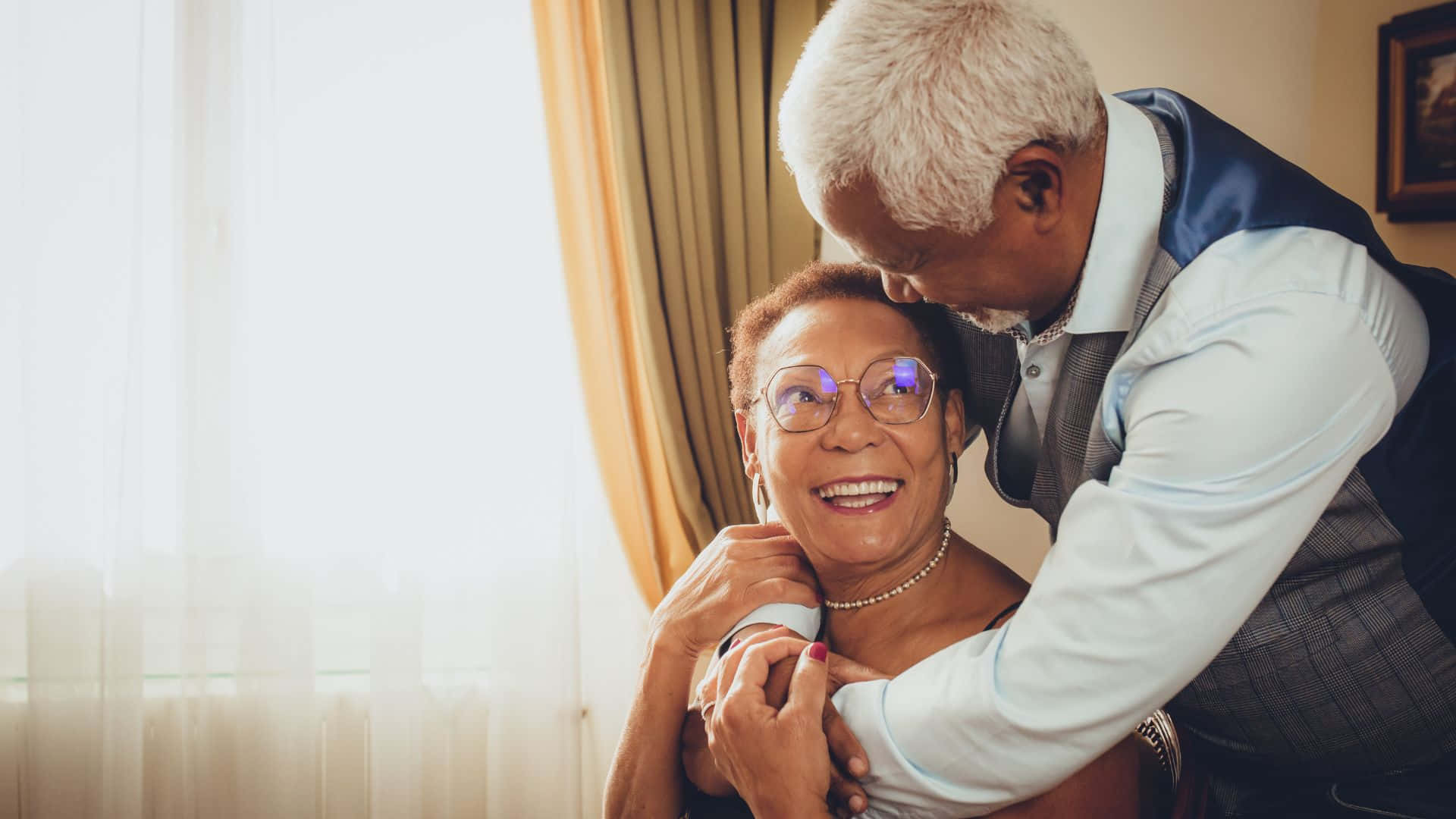 Beautiful Love 桌布 壁紙 — 一對年長夫婦在光線溫暖、帶有柔軟窗簾和金色色調的房間裡溫柔擁抱。