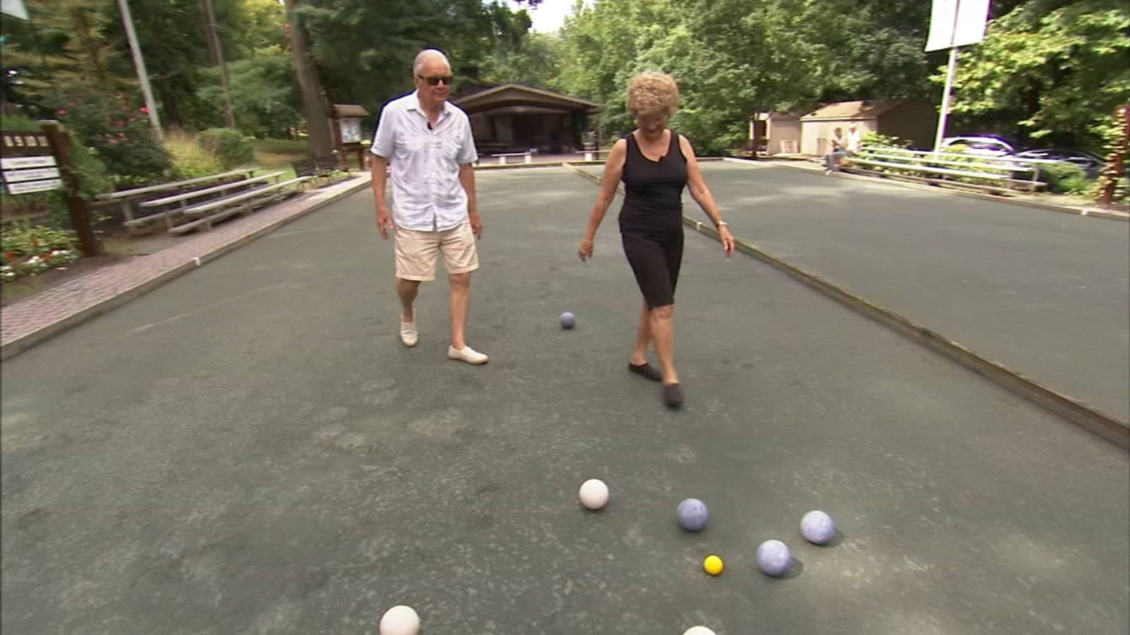 balls 桌布 壁紙 — 一對年長夫婦在鋪砌的球場上散步，四周樹木環繞，他們正在玩色彩繽紛的法式滾球。