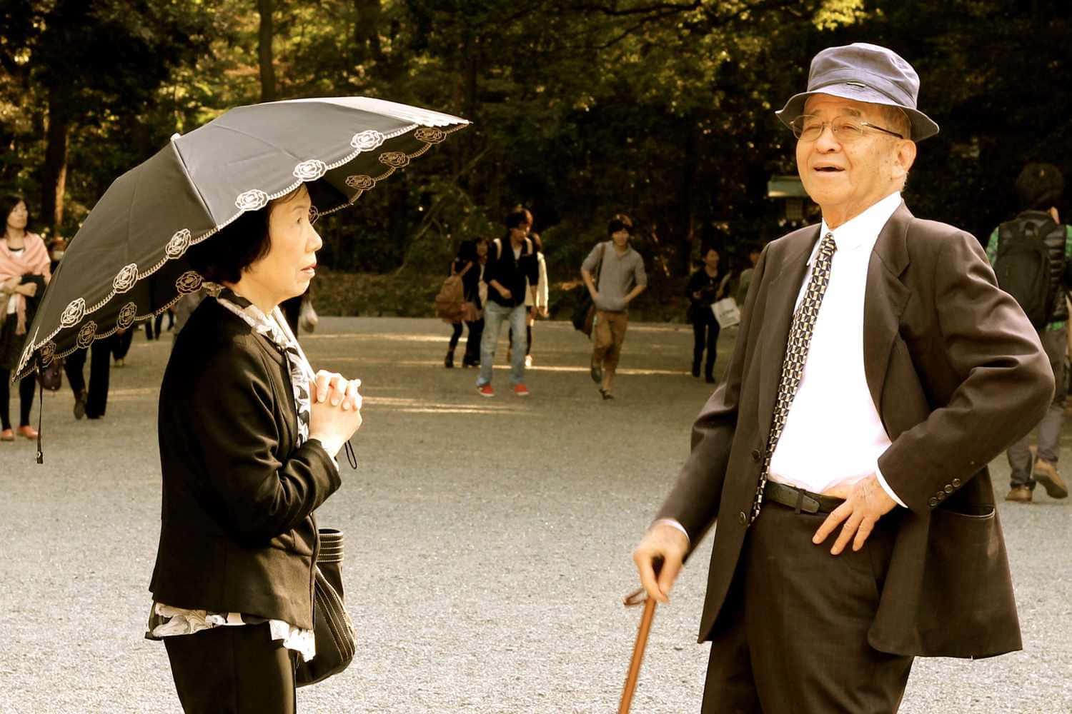 日式 桌布 壁紙 — 一對年長夫婦在陽光明媚的公園裡共享寧靜時刻，女士手持華麗的雨傘，男士則倚靠著手杖。