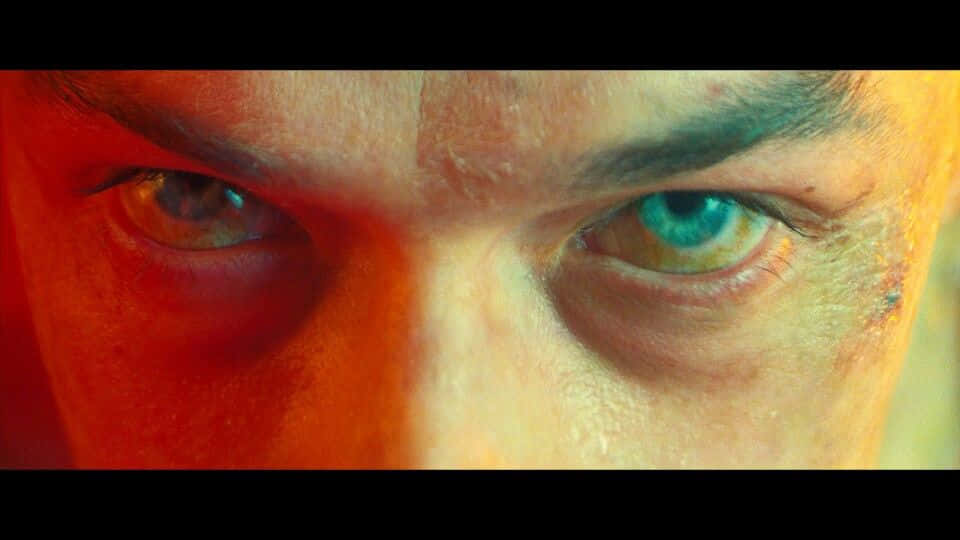 Harry Osborn 桌布 壁紙 — 一對強烈眼睛的特寫，被紅色和黃色燈光分割，其中一隻眼睛發出藍綠色光芒。