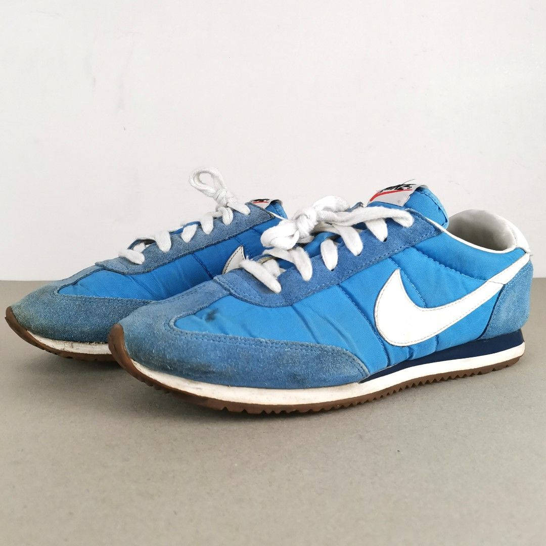  壁紙 — 一對復古藍色Nike運動鞋，配有白色鞋帶和Swoosh標誌，放在中性灰色表面上，背景是純白色牆壁。